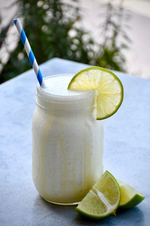 A smoothie in a mason jar with a straw and lime slices on a table.