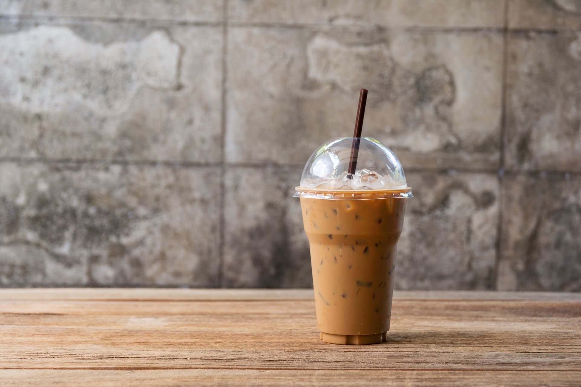 A cup of iced coffee with a straw on a wooden table.