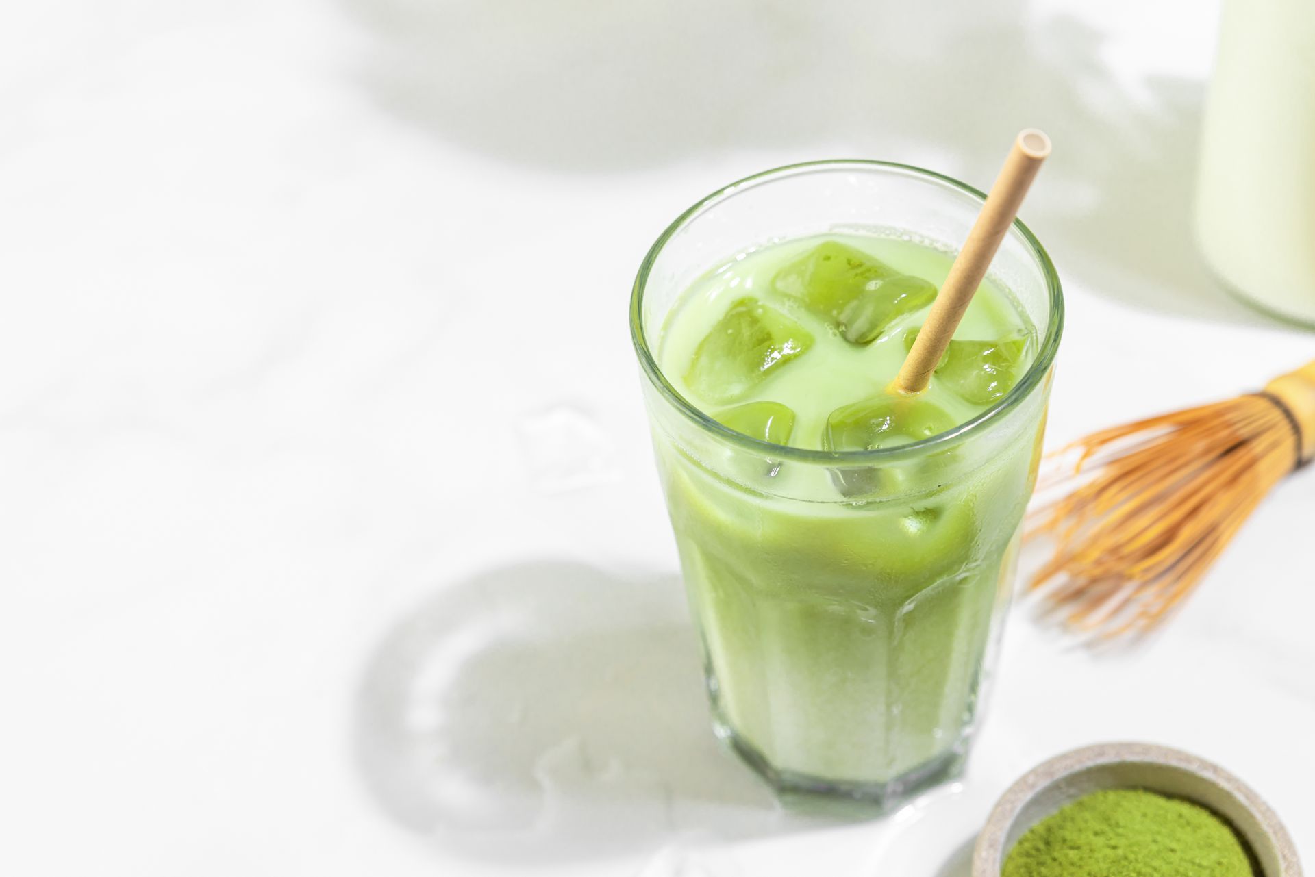 A glass of green tea with ice cubes and a bamboo straw.