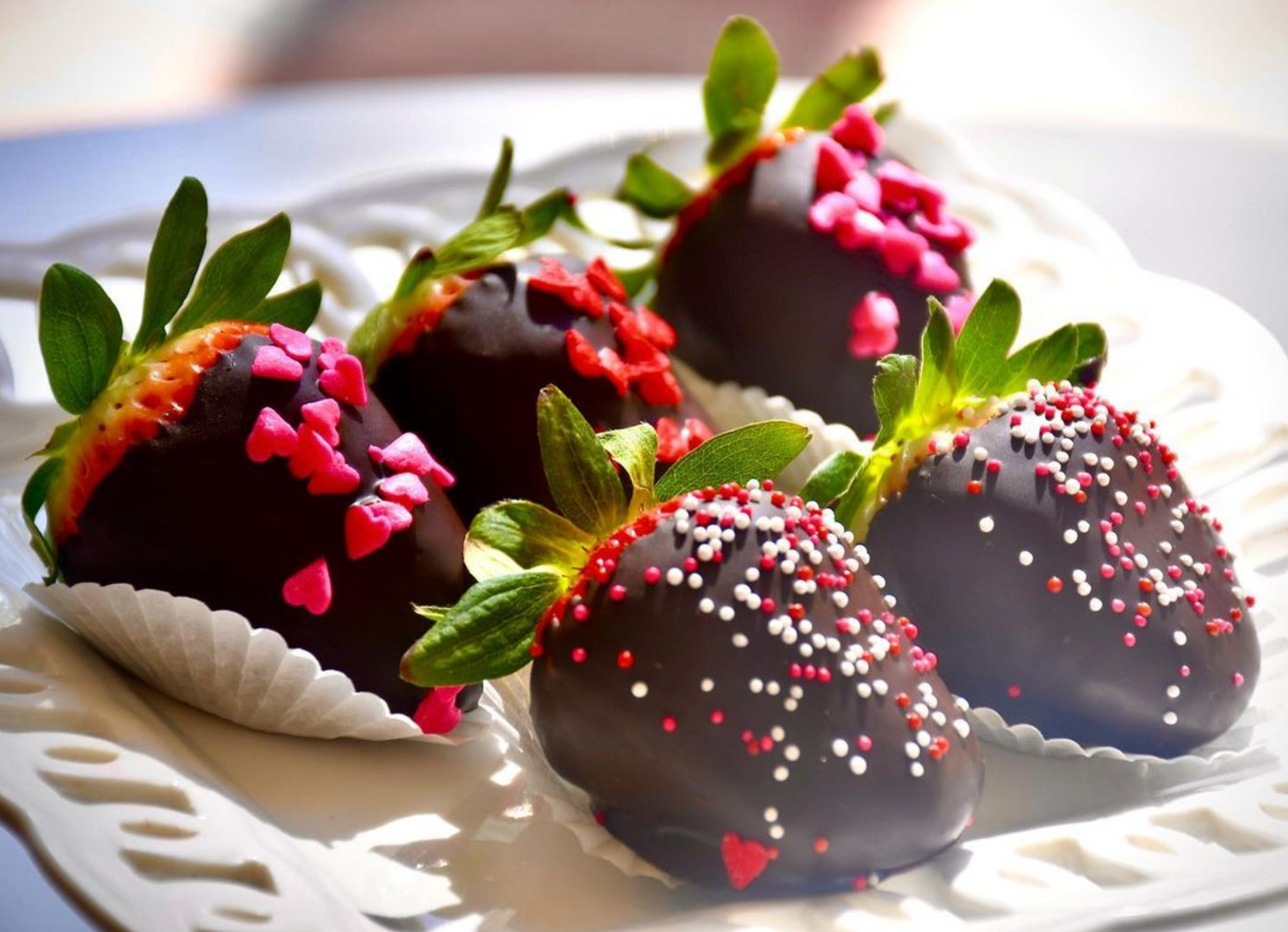 A white plate topped with chocolate covered strawberries and sprinkles