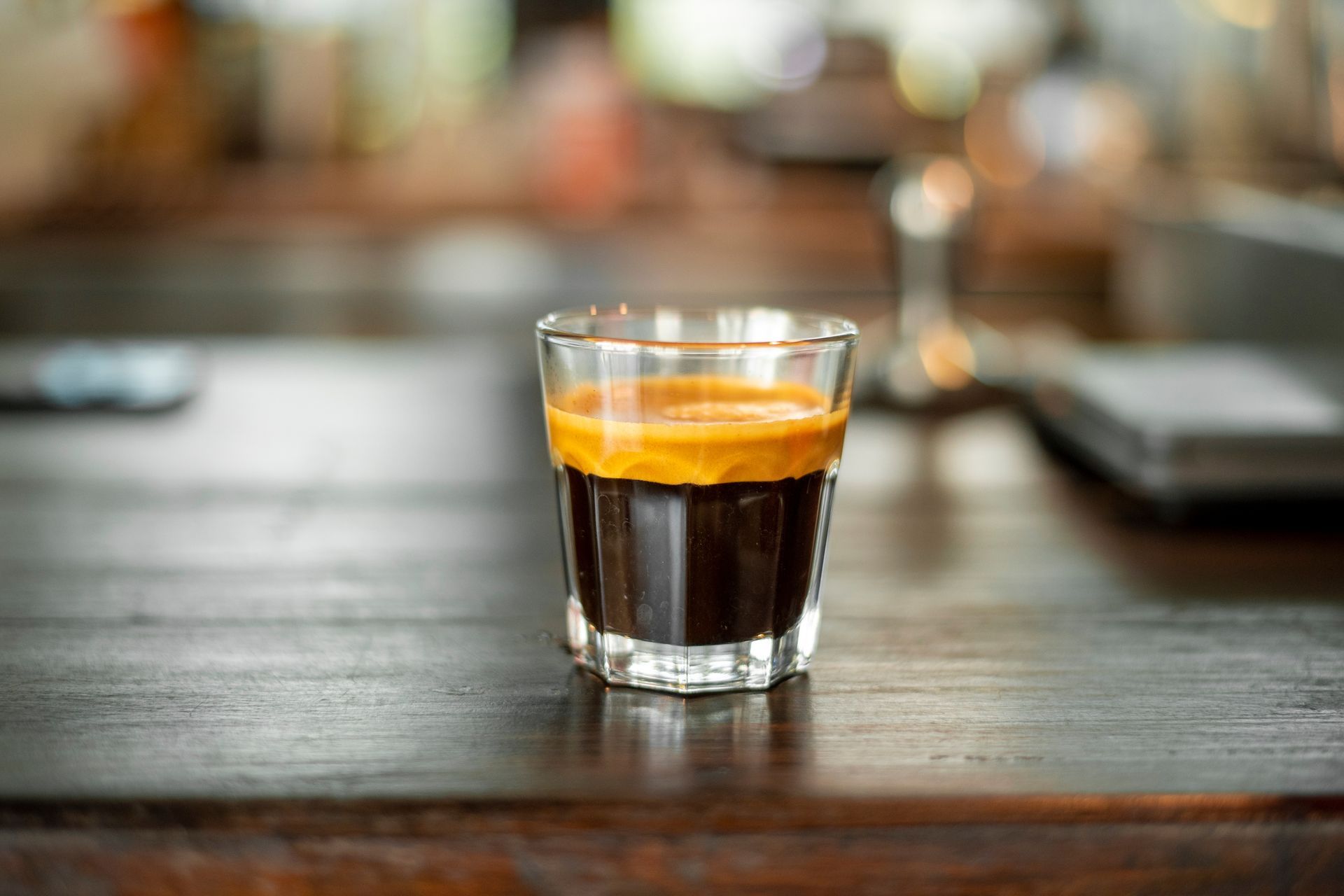 A glass of espresso is sitting on a wooden table.