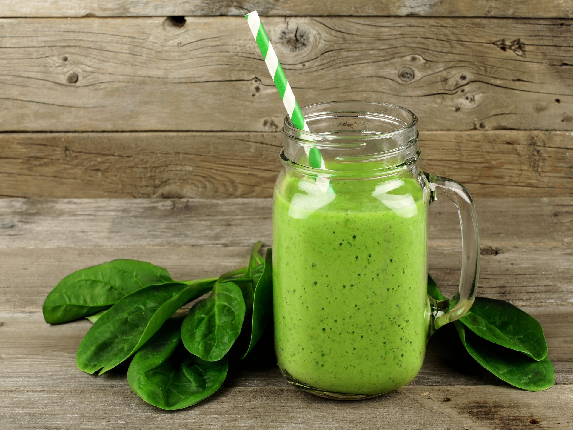 A green smoothie in a mason jar with a straw on a wooden table.