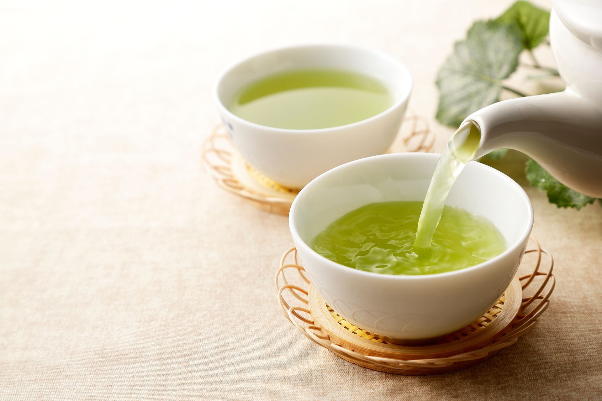 Two cups of green tea are being poured from a teapot.