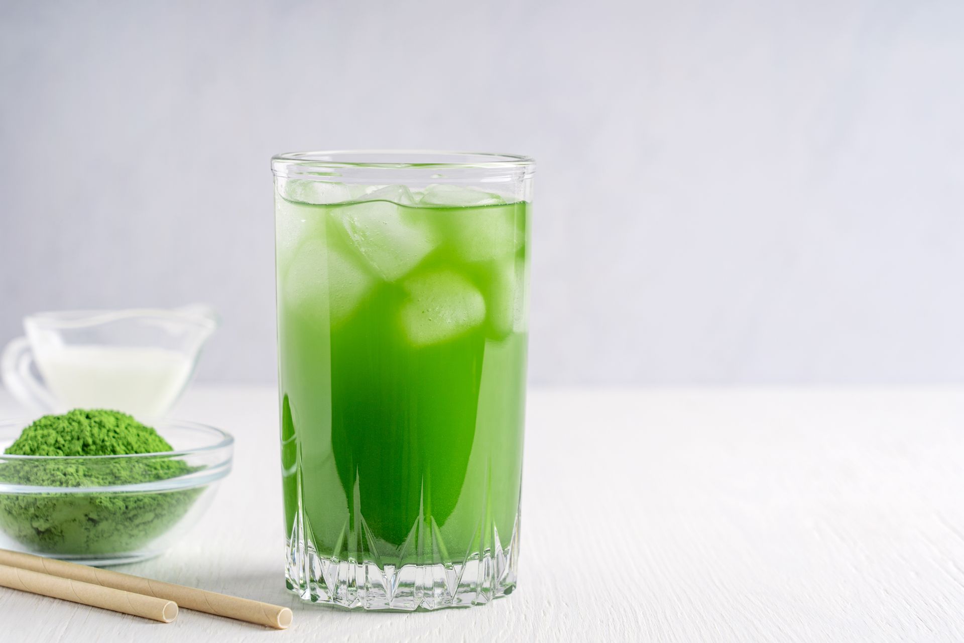 A glass of green tea with ice and milk on a table.