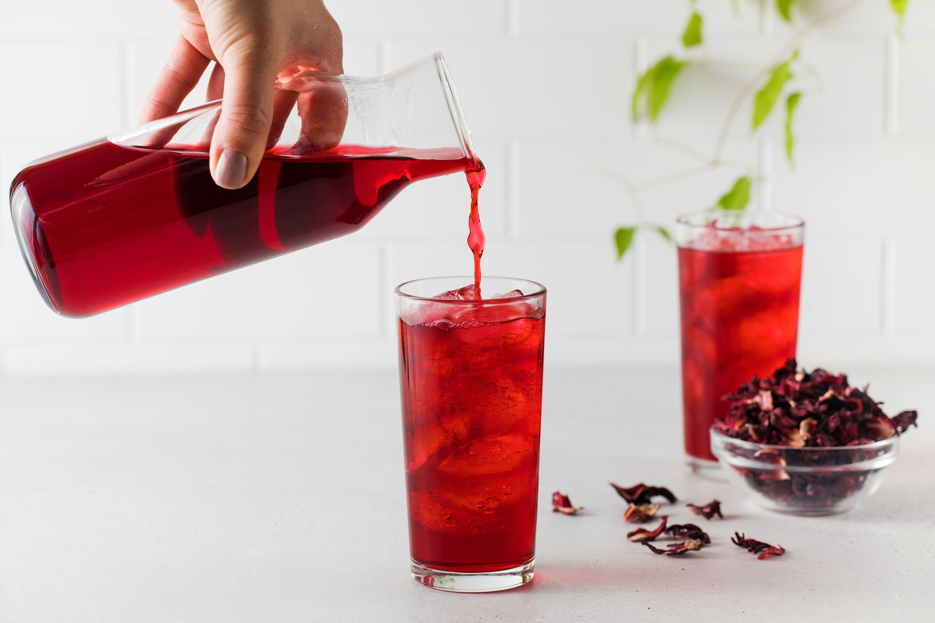 A person is pouring hibiscus tea into a glass.