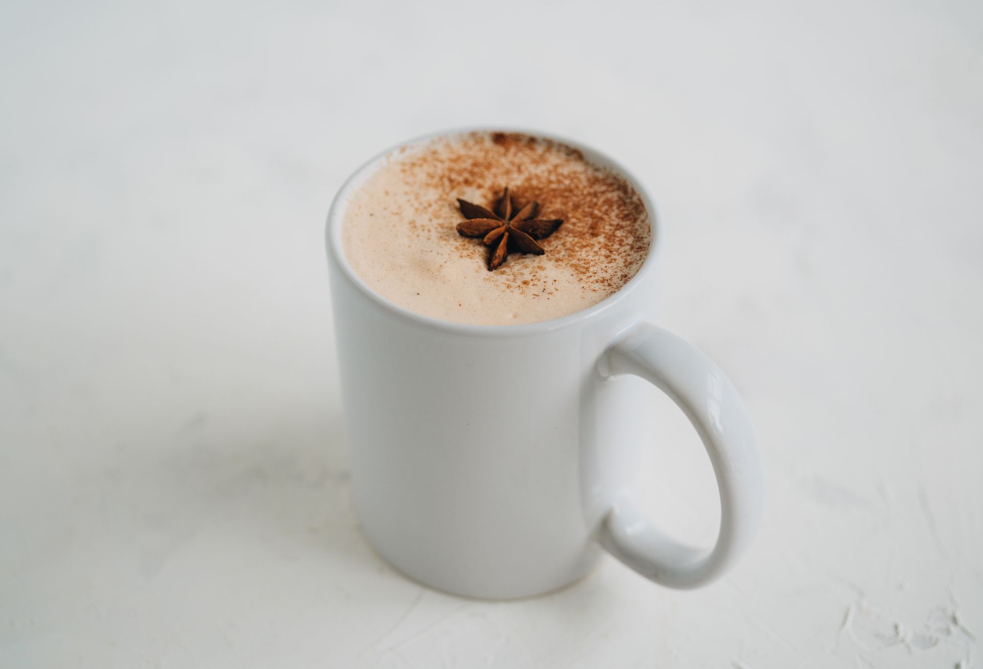A white mug filled with a cappuccino with anise on top.