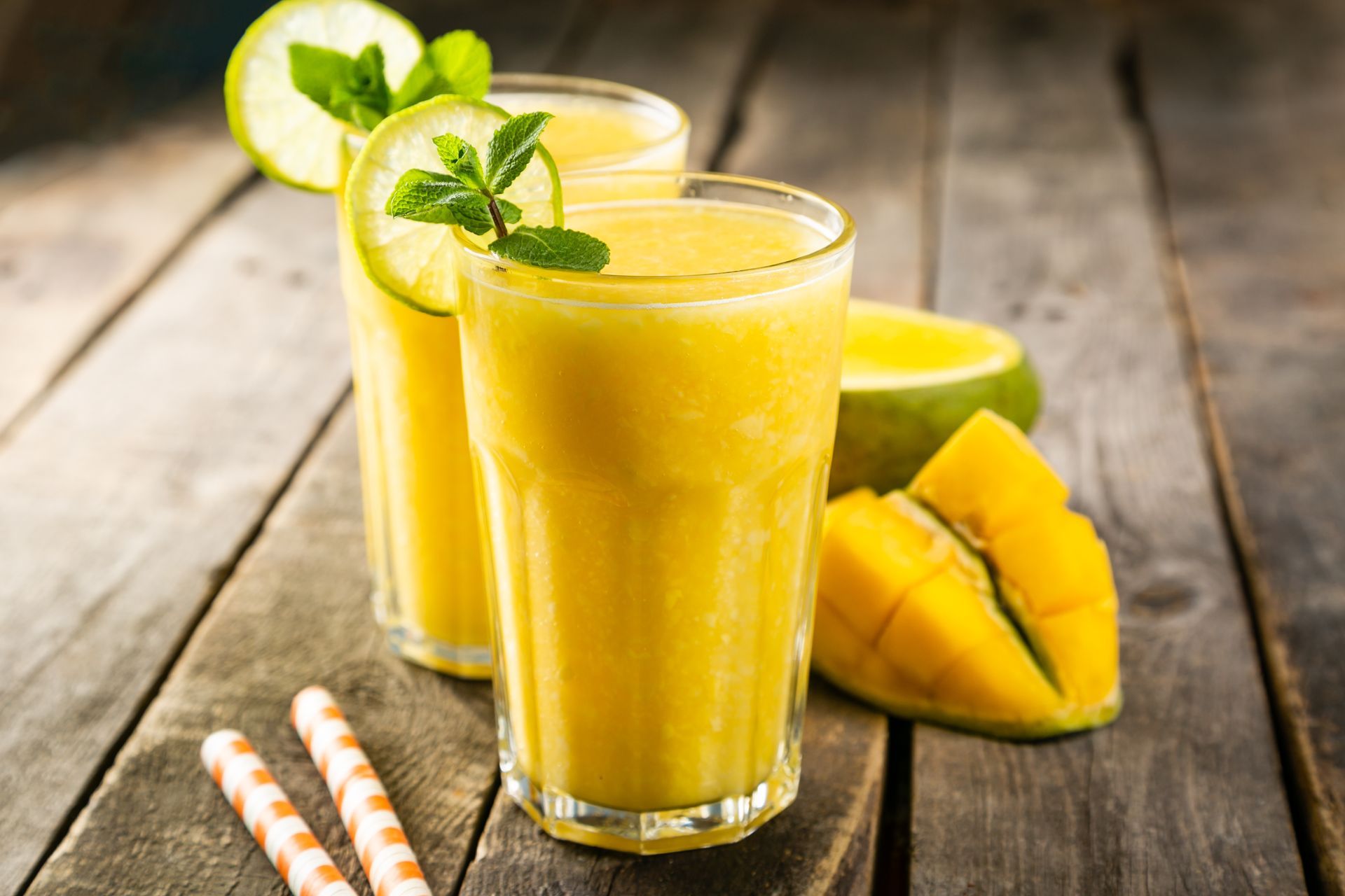 Two glasses of mango juice with straws on a wooden table.