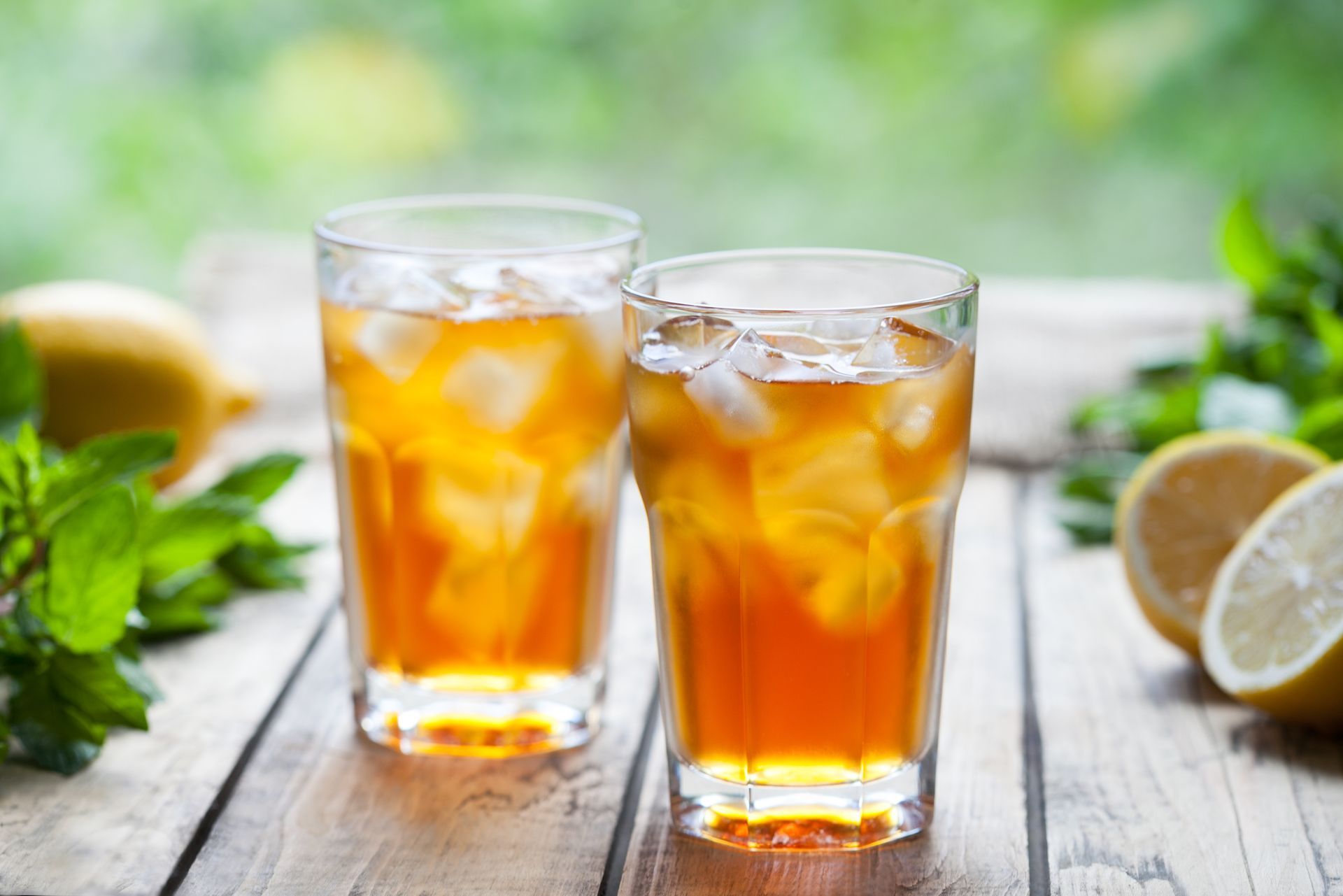 Two glasses of iced tea with ice cubes on a wooden table.