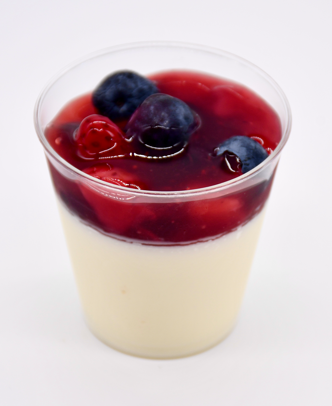 A cup of panna cotta with berries on top of it