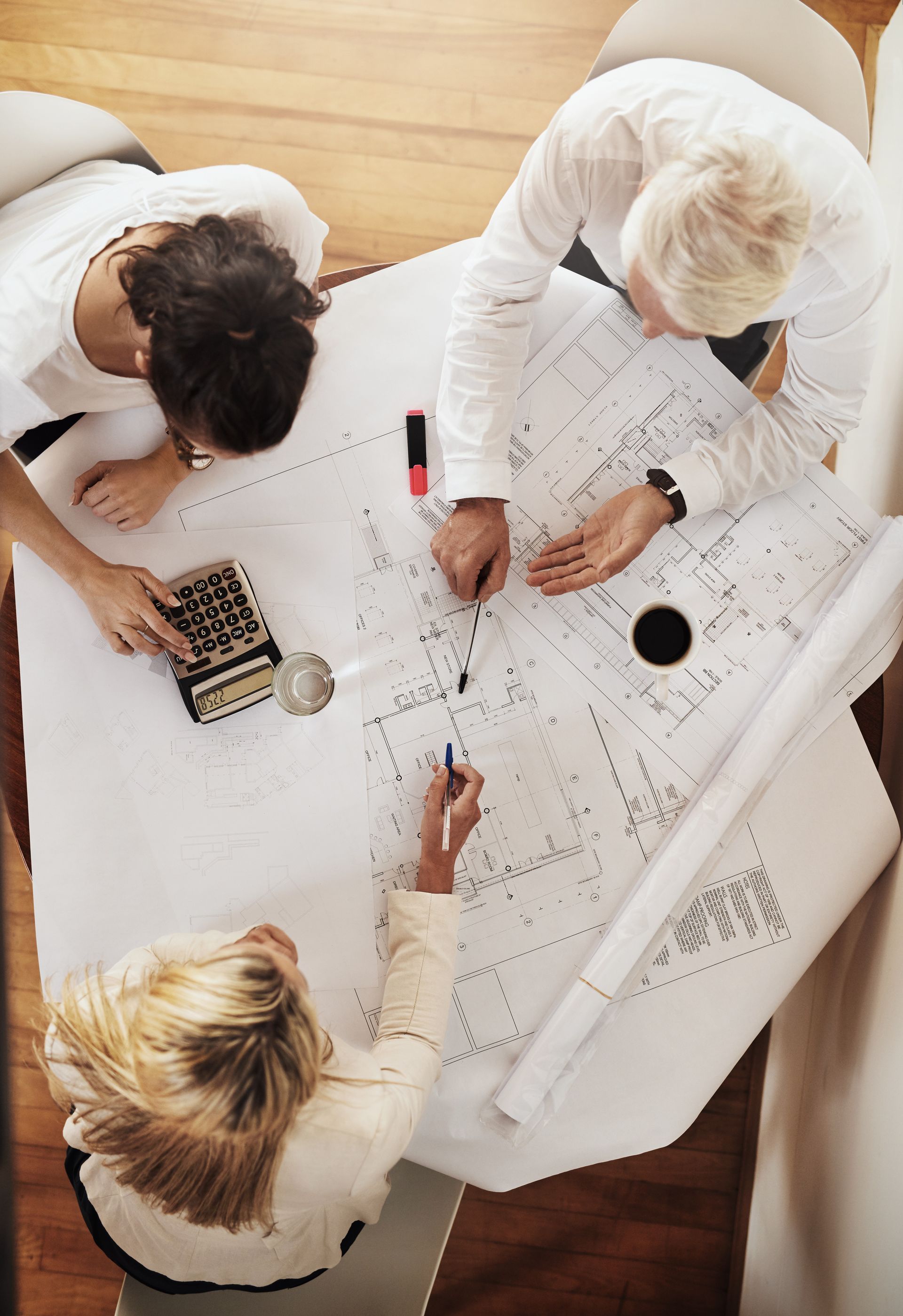 Three people collaborating over a large white sheet covered in sketches and notes on a table