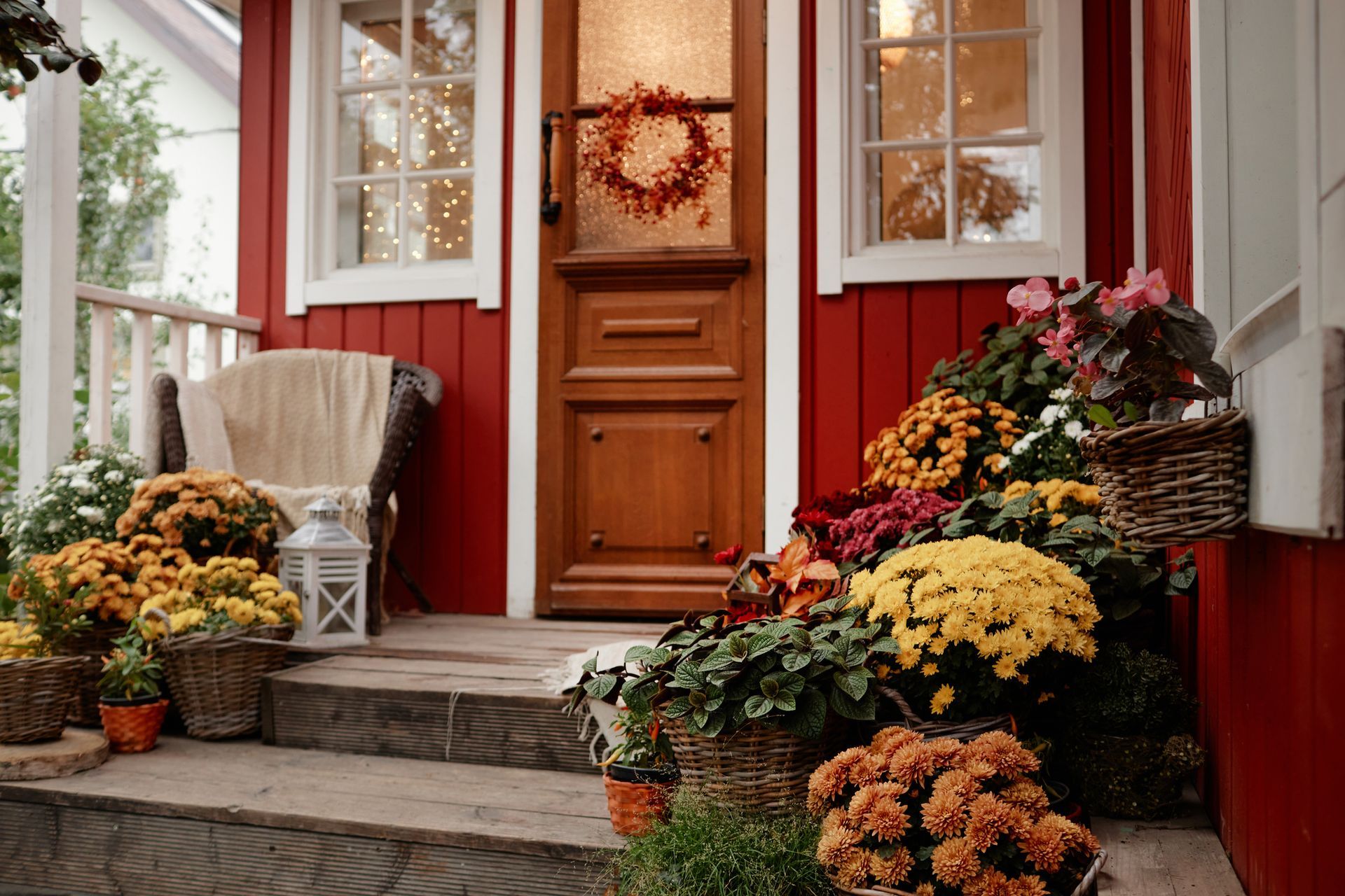 Front porch with red siding, wooden door, wreath, and autumn flower pots on the steps