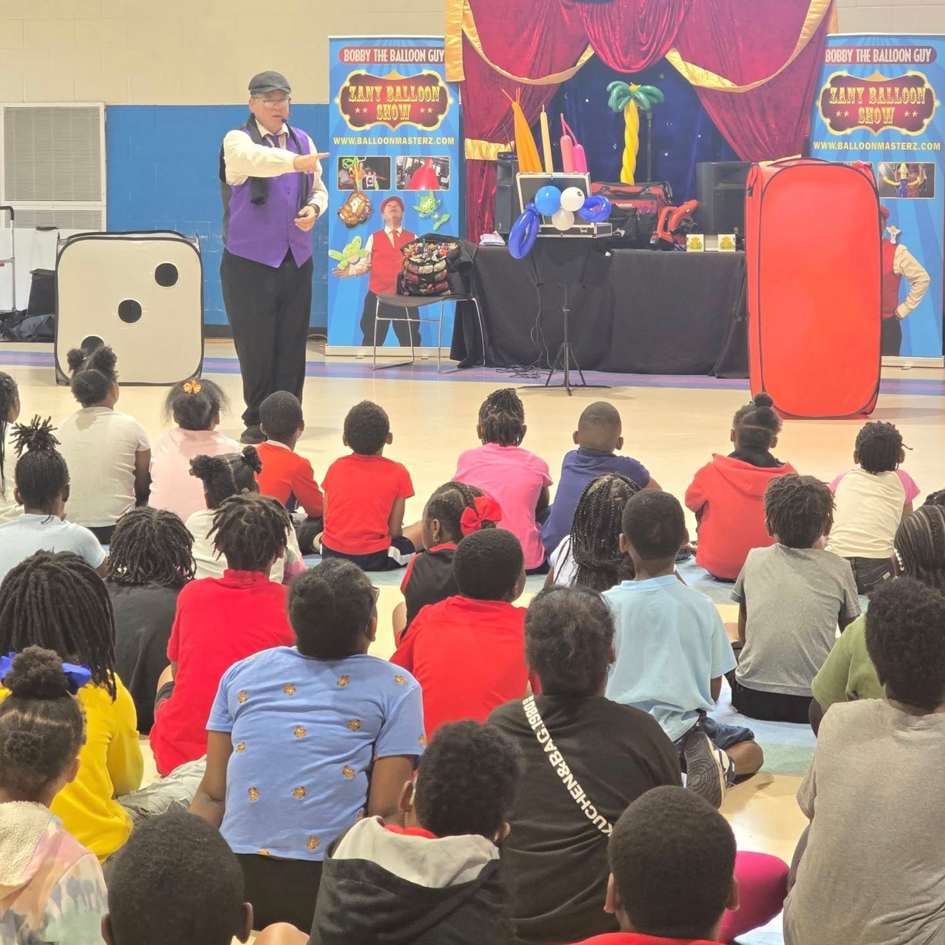 Magician performs for seated children. Stage backdrop, equipment and props present.