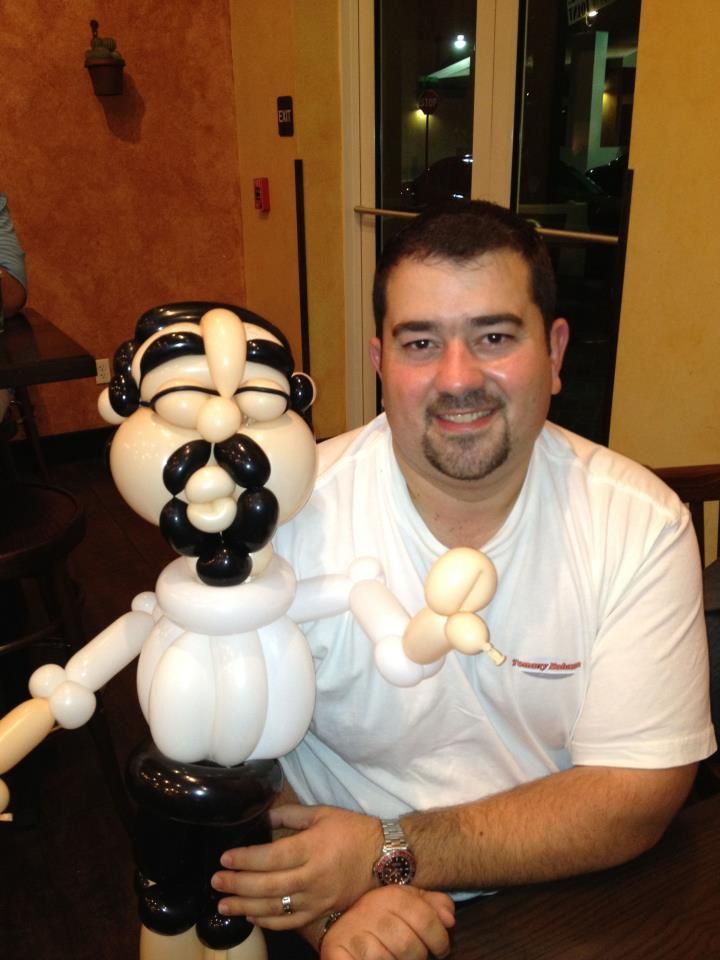 Girl holding balloon sculpture of a mermaid; wearing white shirt with black bow; smiles in indoor setting.