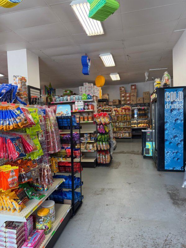Convenience store aisle with colorful snacks and drinks, refrigerators, and fluorescent ceiling lights