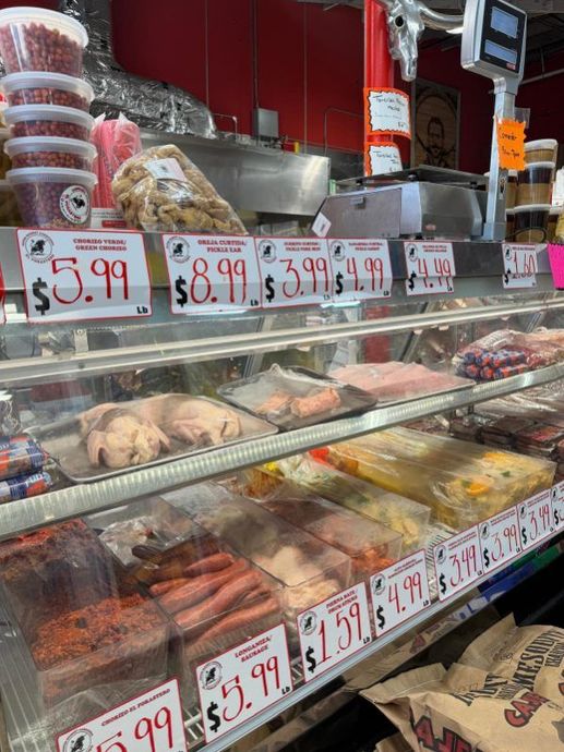 Deli meat counter with trays of meats and handwritten price signs in a grocery store