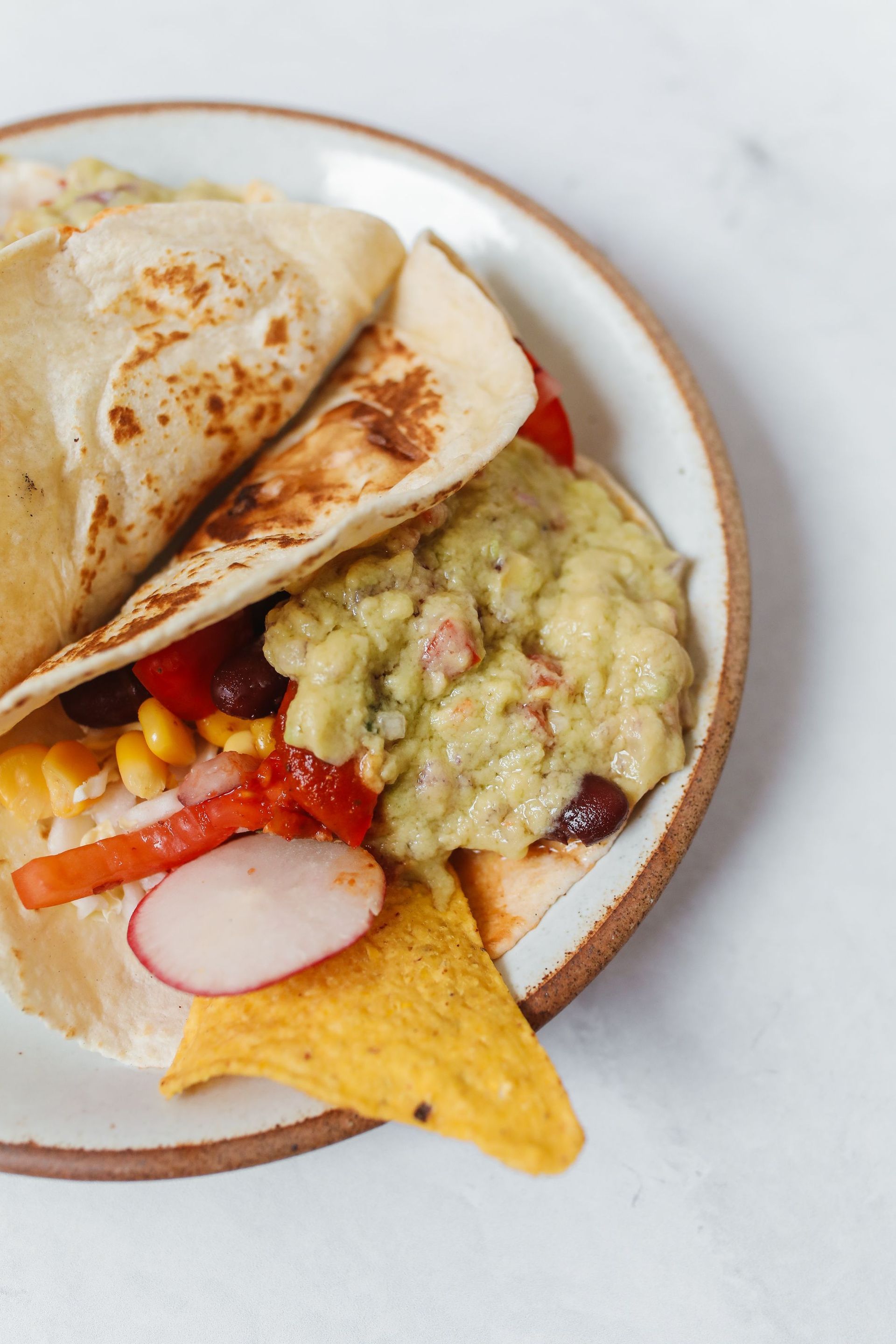 Plate of assorted Mexican food: tacos, guacamole, tortilla chips, and corn with radishes.