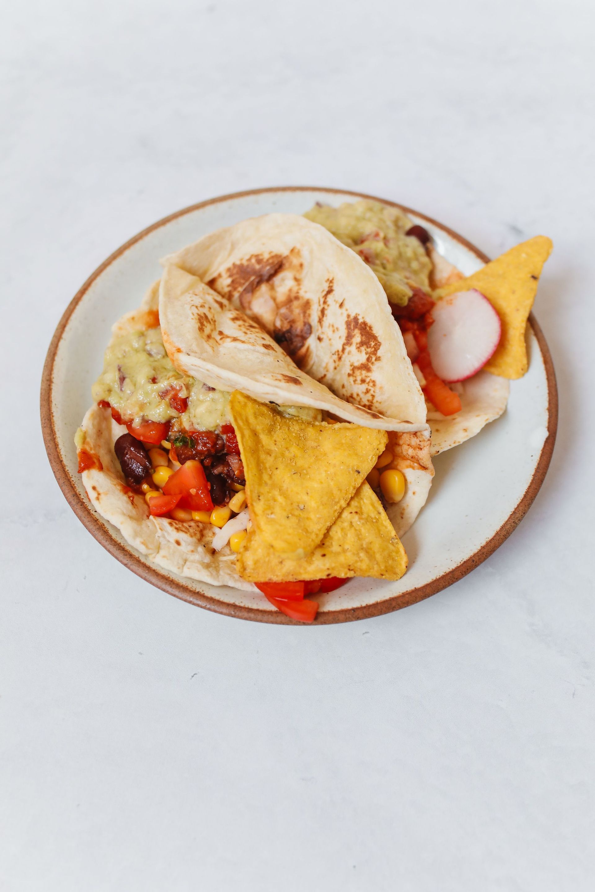 Plate of assorted snacks with tortilla chips, hummus, pita, and sliced radish on a white background