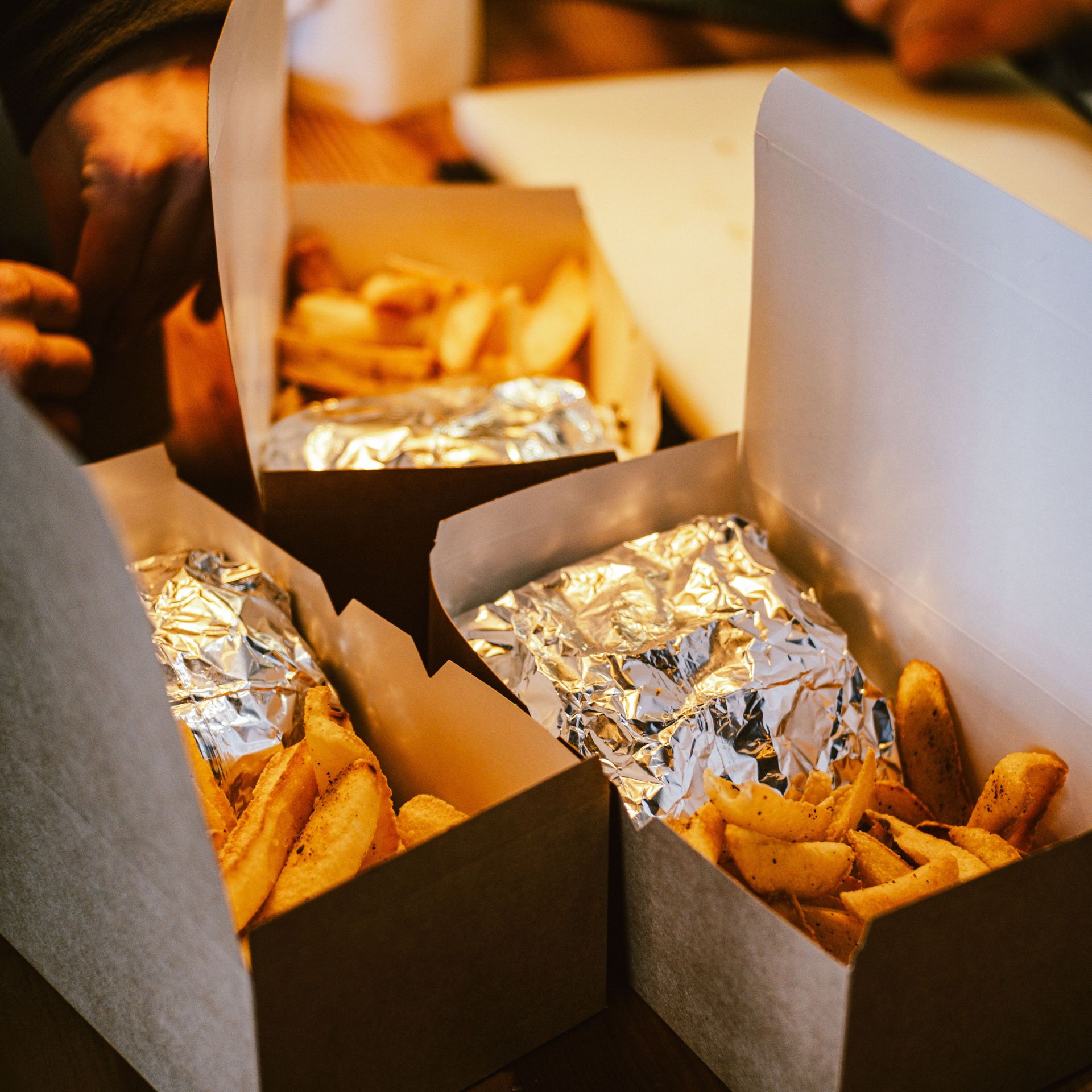 Takeout boxes filled with fries and foil-wrapped sandwiches on a table