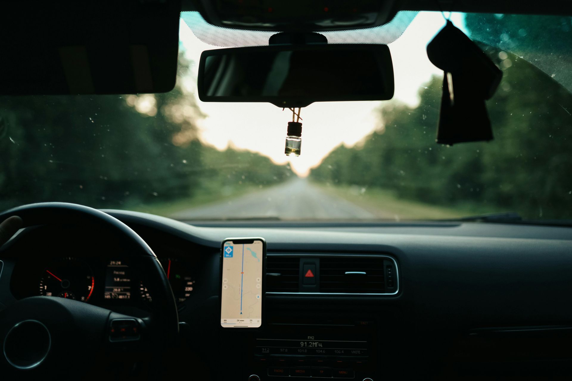 Interior car view, dashboard, steering wheel, phone with GPS, looking down a road through windshield.