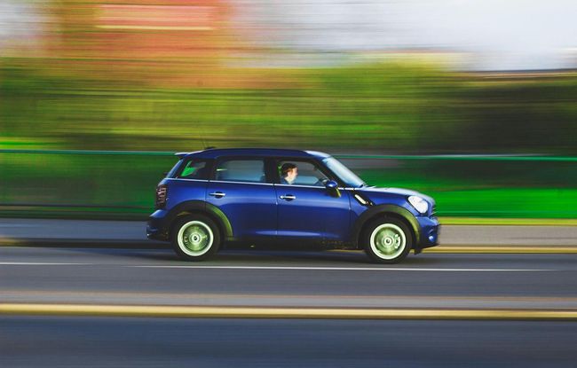 Blue Mini Cooper driving fast on a road, with motion blur effect.