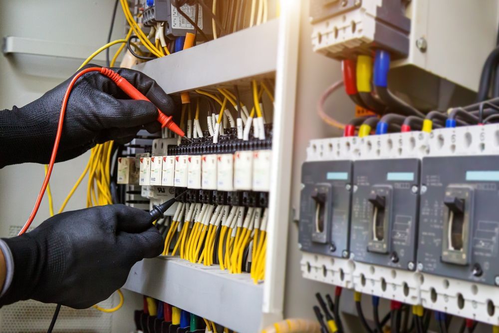 Gloved technician wiring an electrical panel with breakers and yellow cables in a control cabinet