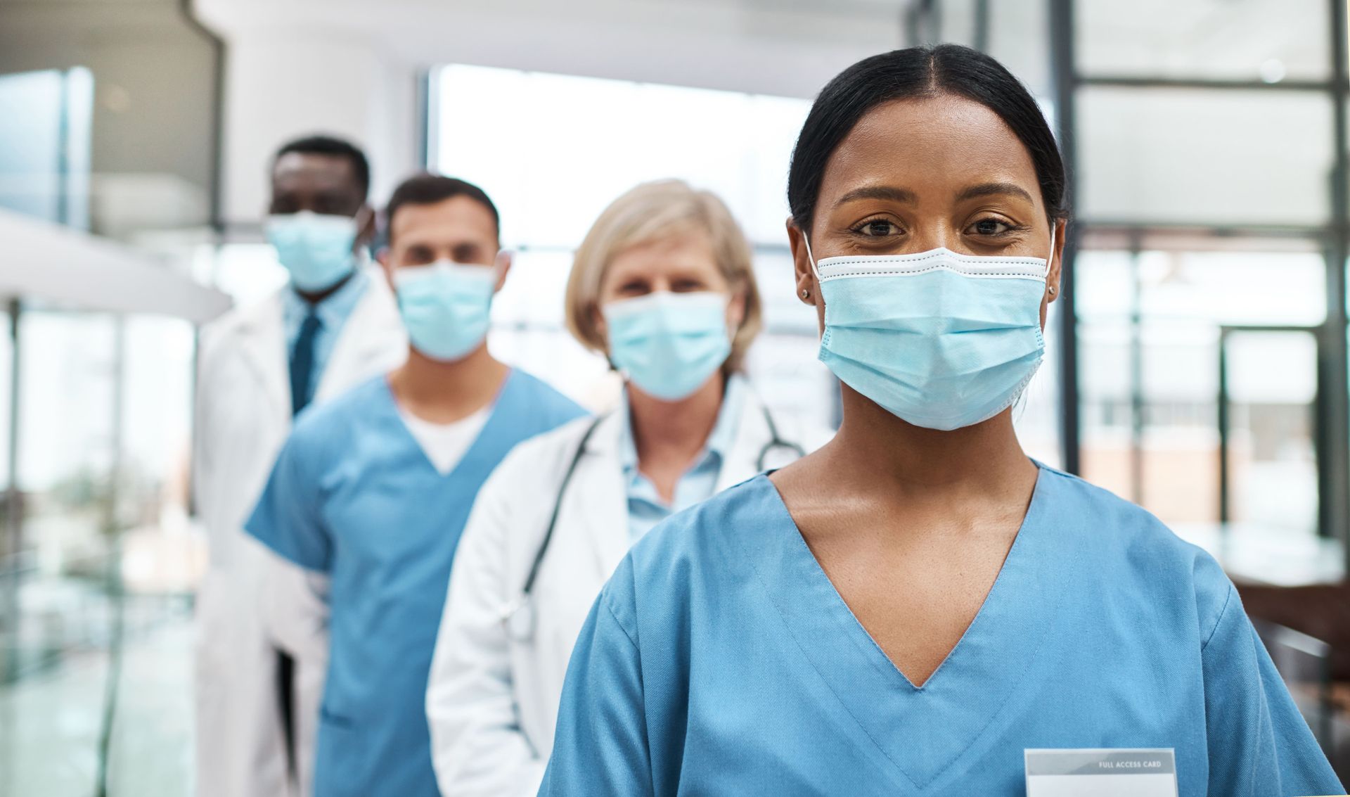 Profissionais de saúde com uniformes cirúrgicos e máscaras estão em um corredor de hospital.