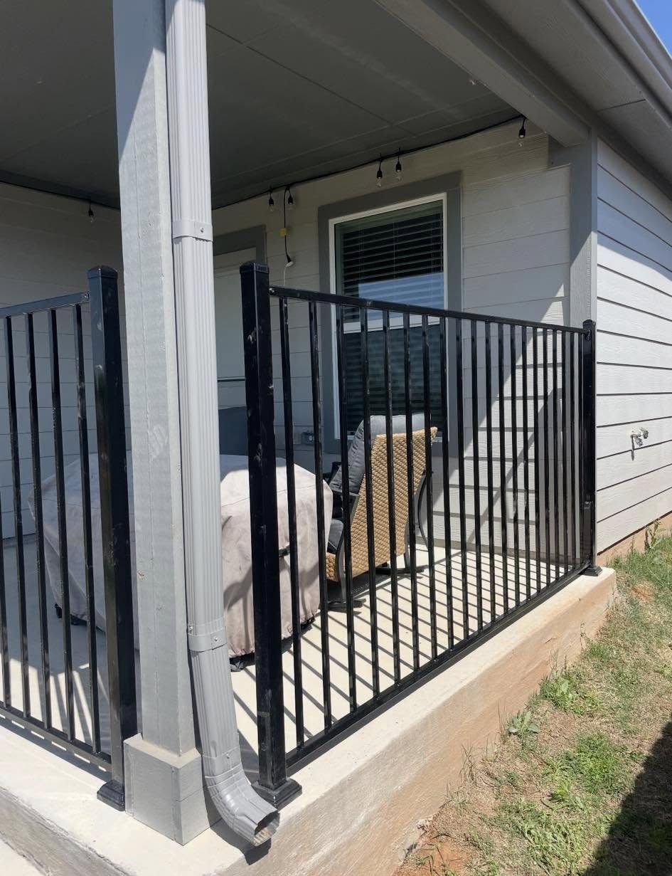 Black metal railing enclosing a concrete patio, next to a building's exterior with gray siding.