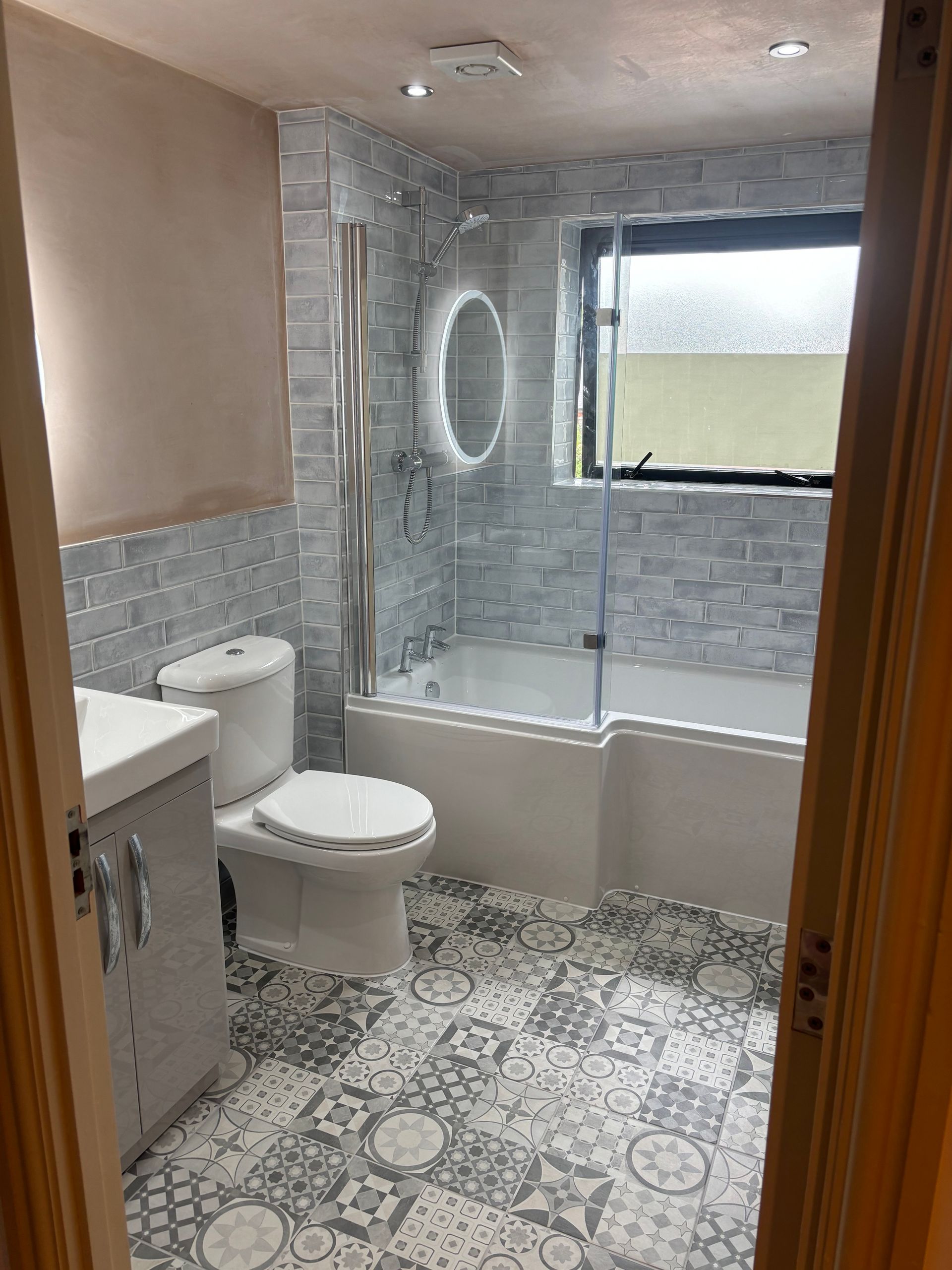 Small bathroom with patterned tile, tub-shower, toilet, and sink in a beige and gray interior.