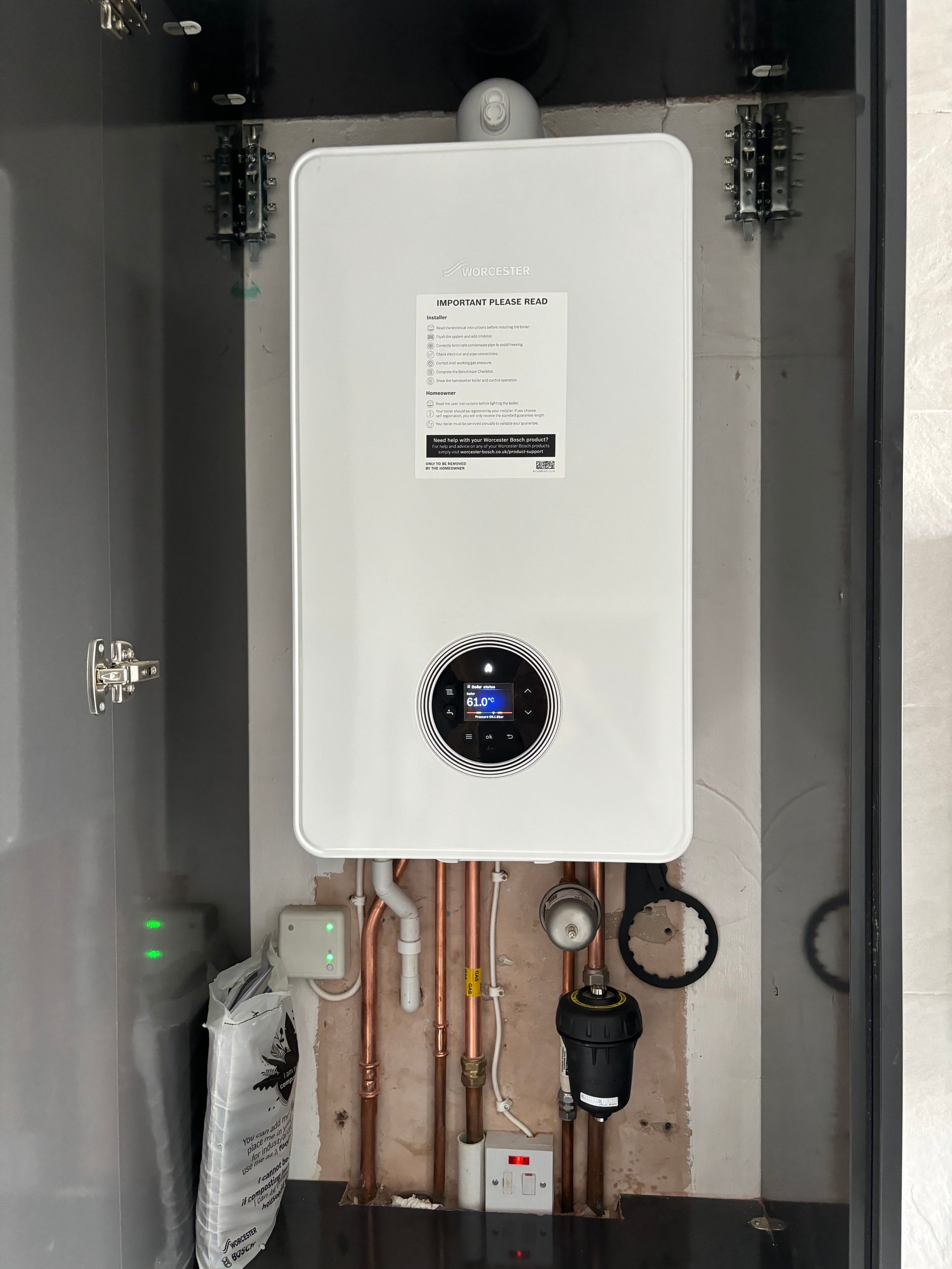 White wall-mounted boiler or water heater in a utility closet with pipes and valves below.