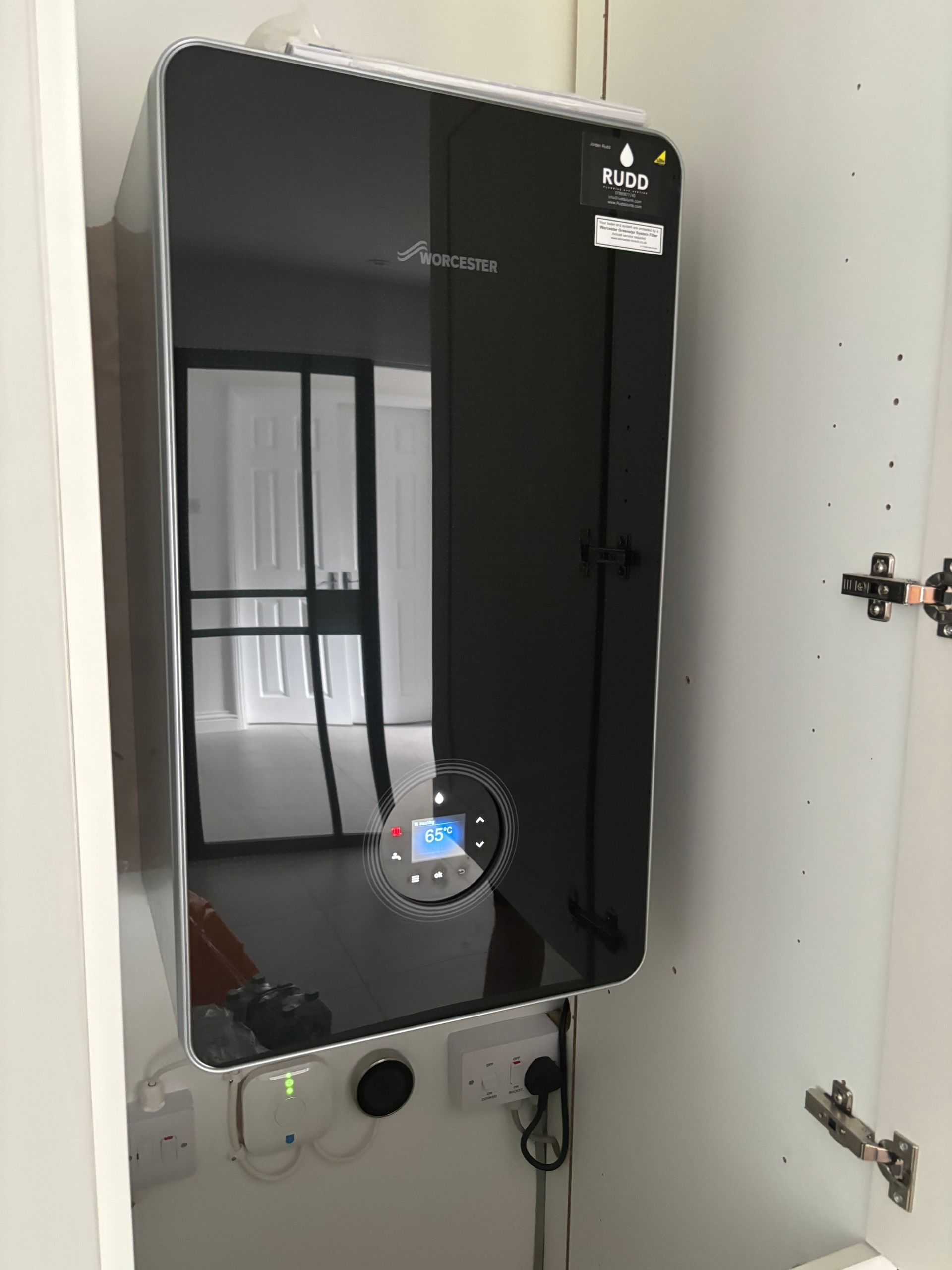 Black wall-mounted smart mirror/control panel in a cabinet, with cords below and open hinges on the right.