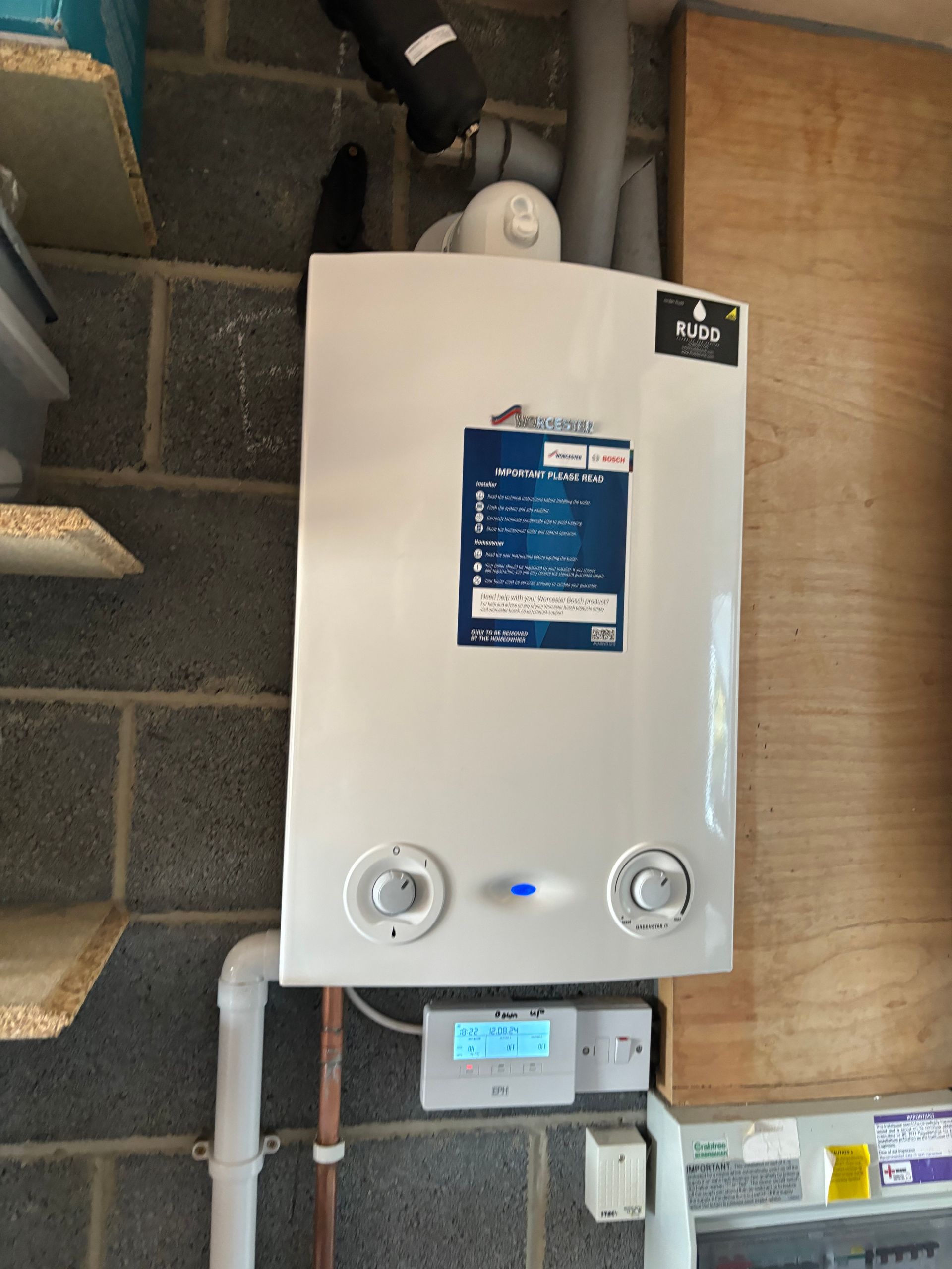 Wall-mounted white water heater with blue label and control knobs in a utility room.