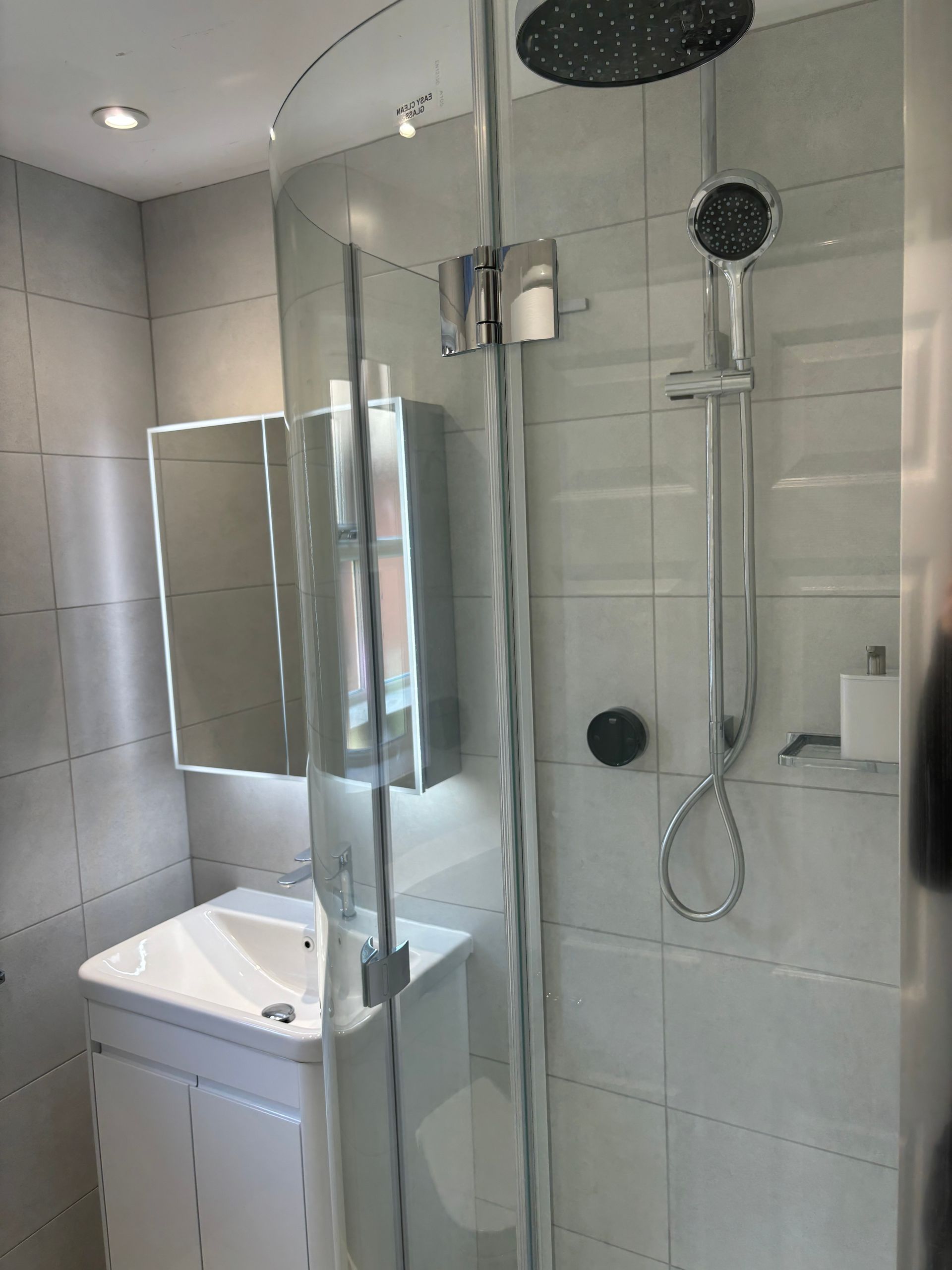 Modern bathroom shower with glass partition, wall-mounted showerhead, and sink cabinet on the left.