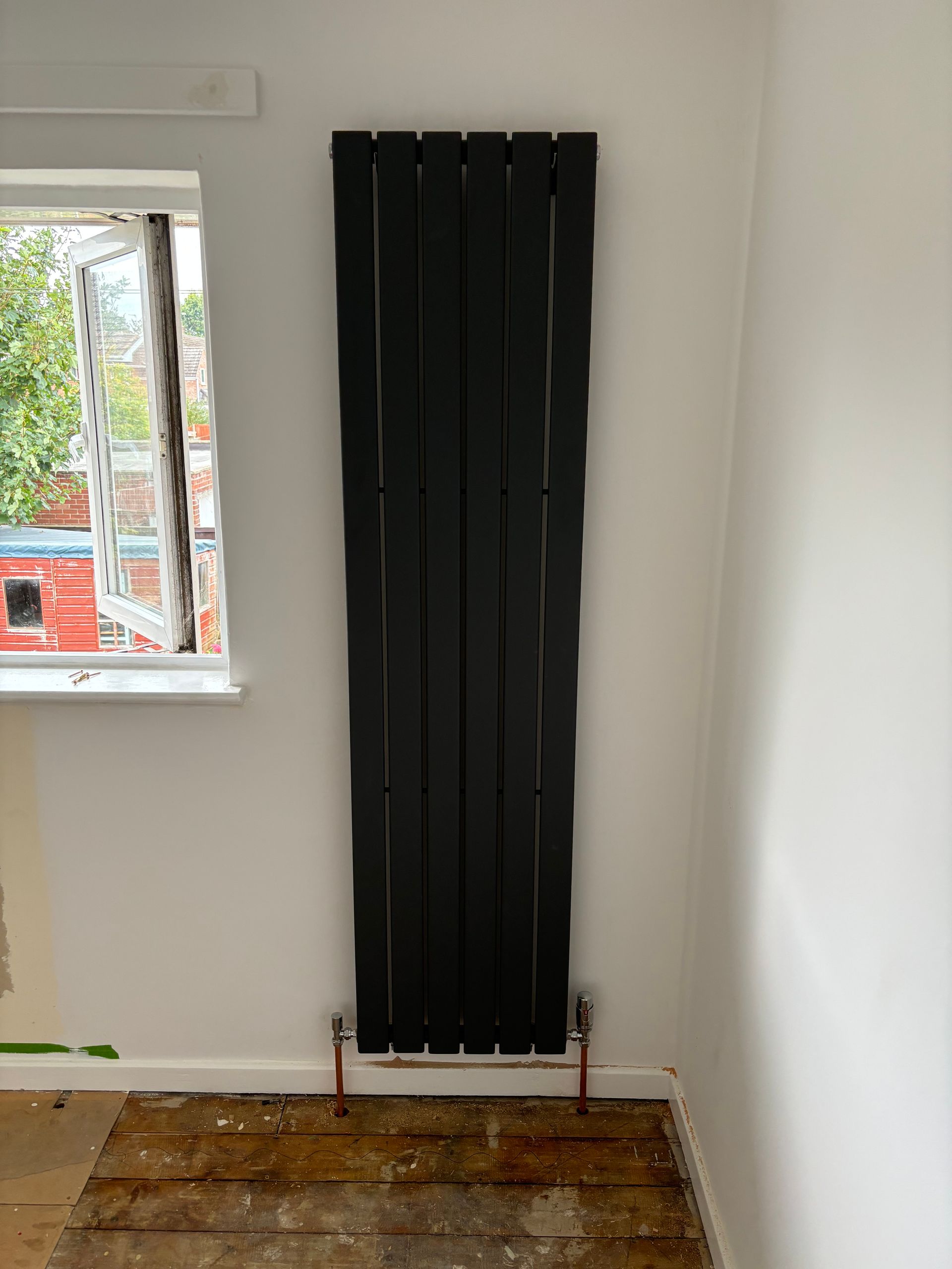 Tall black radiator on a white wall in a sparsely furnished room beside a window