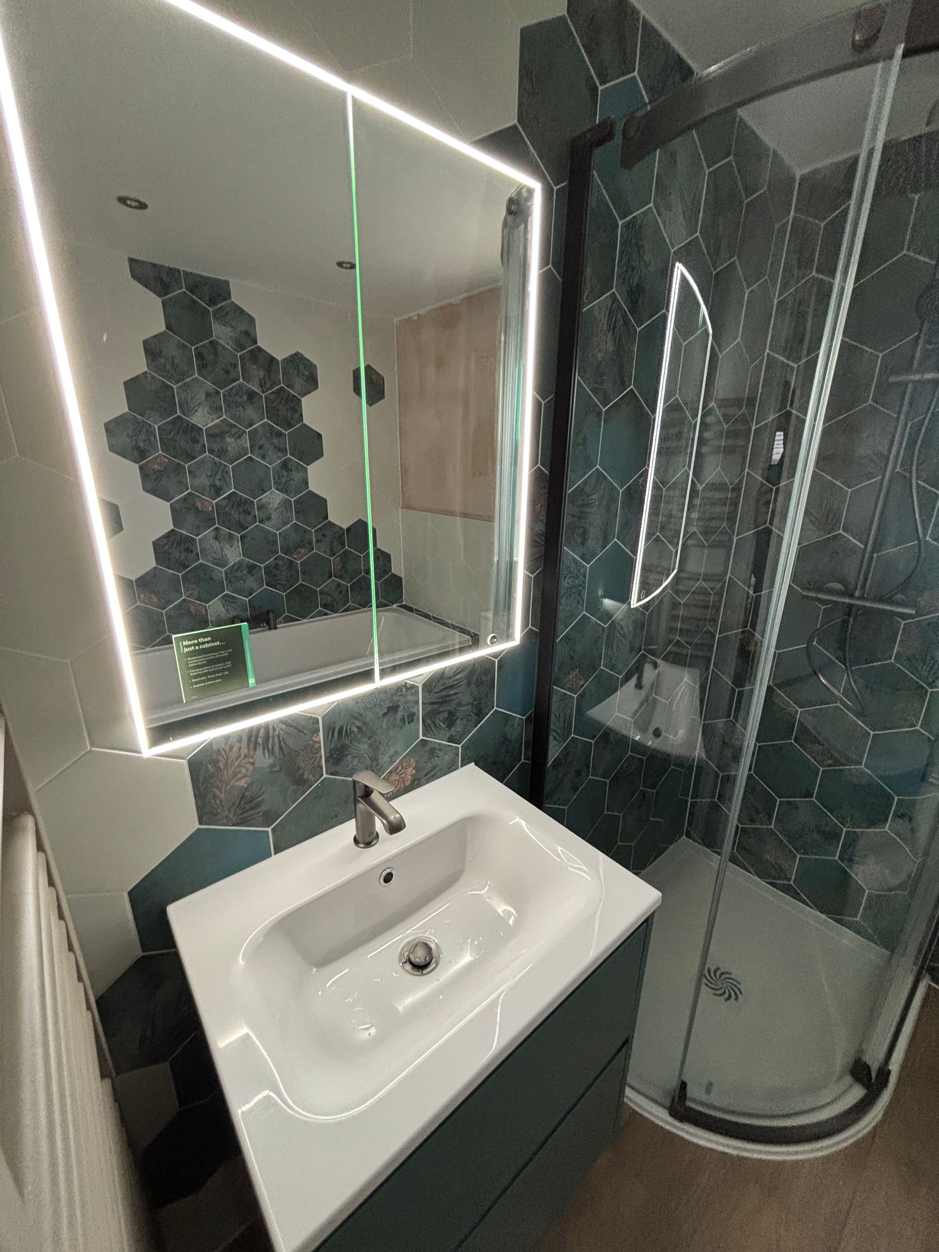 Modern bathroom with vessel sink, illuminated mirror, and glass shower with dark tile accents