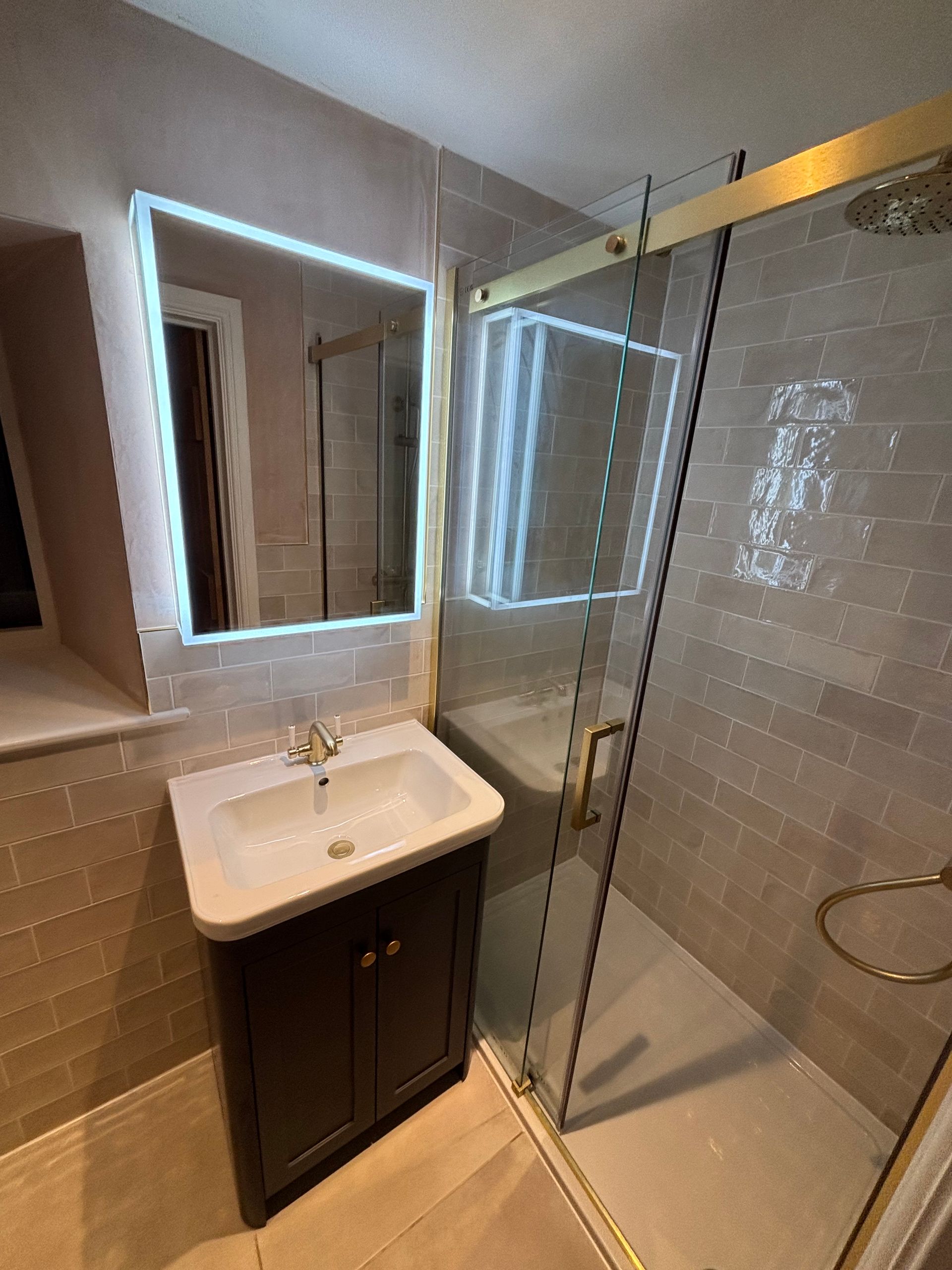Compact bathroom with lit mirror, white sink vanity, and glass shower enclosure