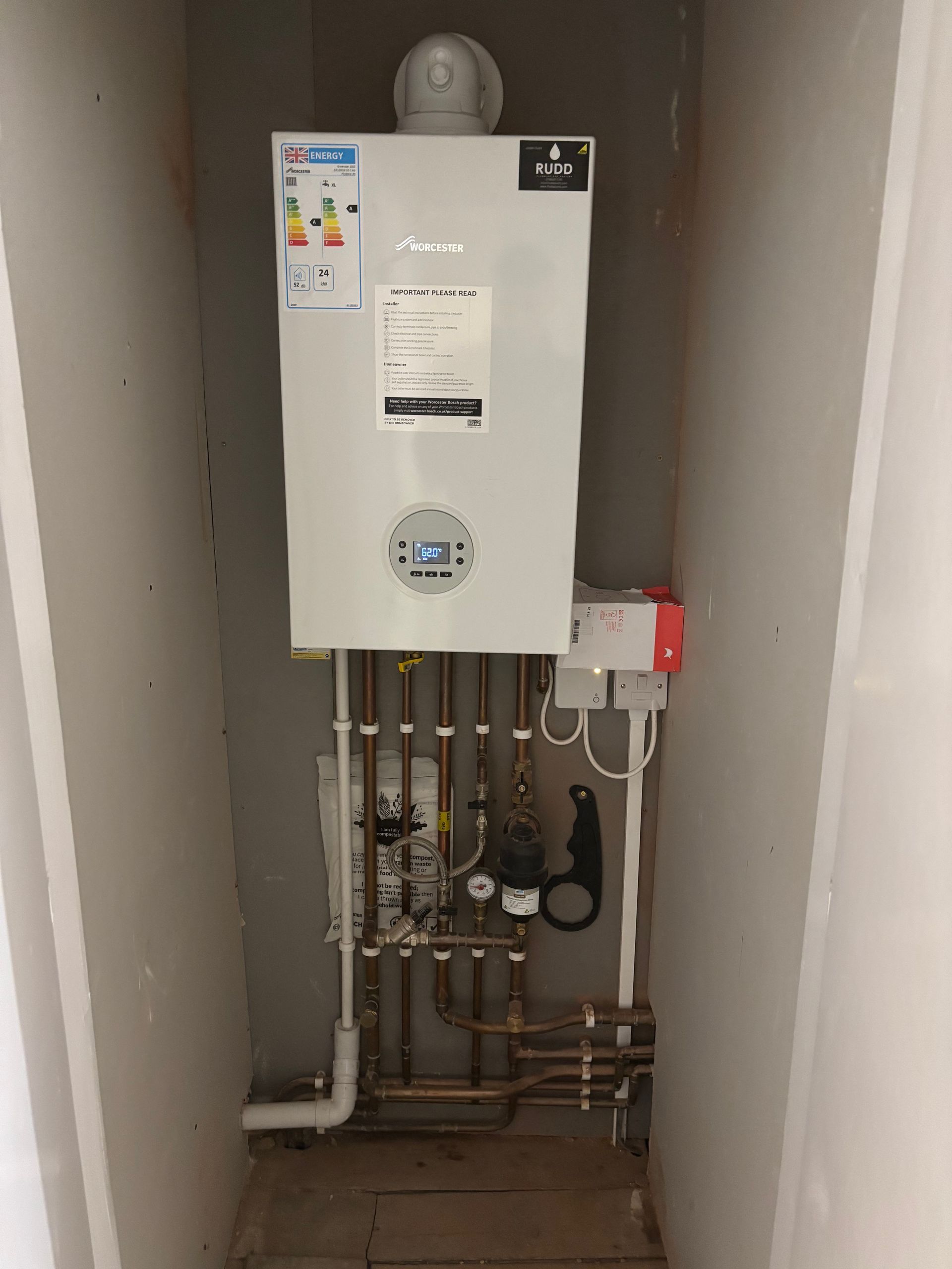 Wall-mounted white gas water heater with exposed pipes and valves in a narrow utility closet