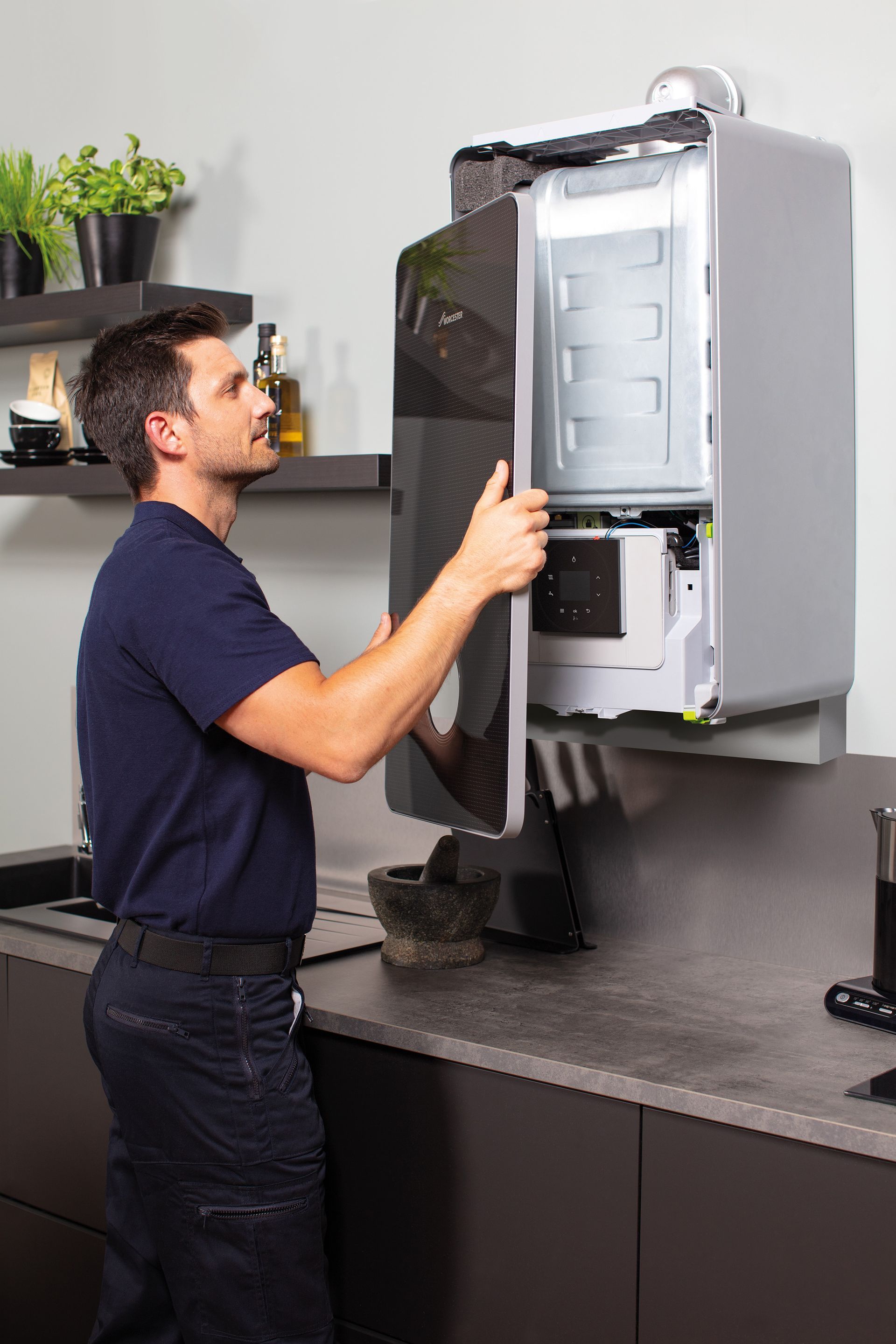 Technician inspecting an open wall-mounted electrical panel in a kitchen-like workspace.