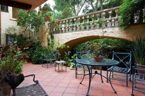 Terracotta patio with wrought-iron furniture, a bridge, and lush greenery.