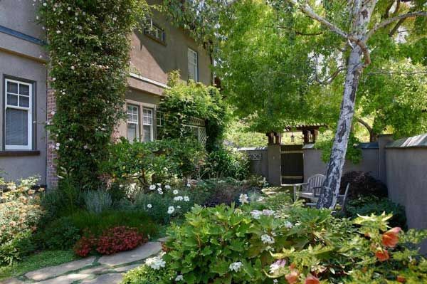 Exterior view of a house surrounded by a lush garden with trees, bushes, and a small patio area.