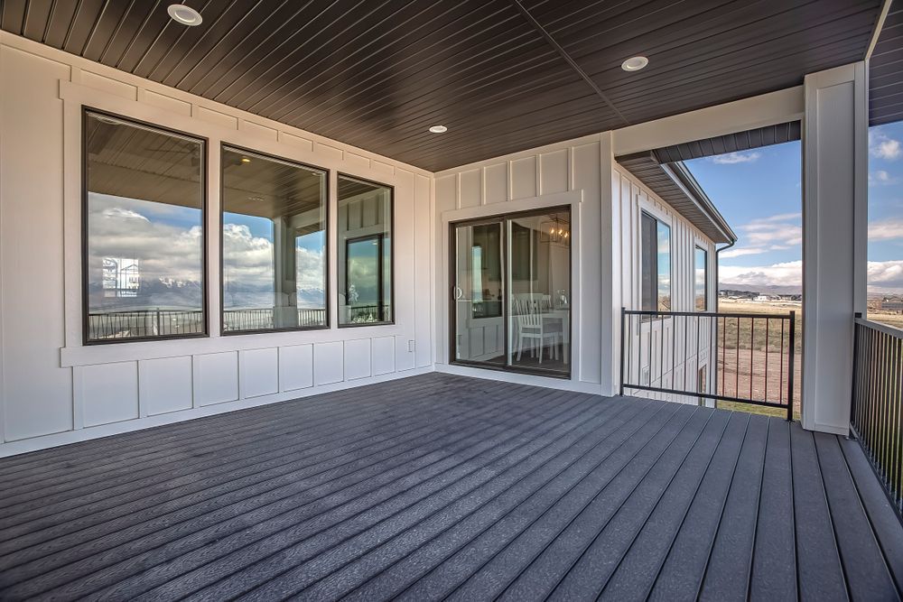 Covered outdoor patio with dark gray floorboards, white siding, and black-framed windows.