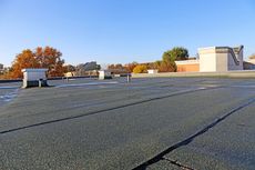 Flat, dark rooftop with several vents and patches, under a clear blue sky.
