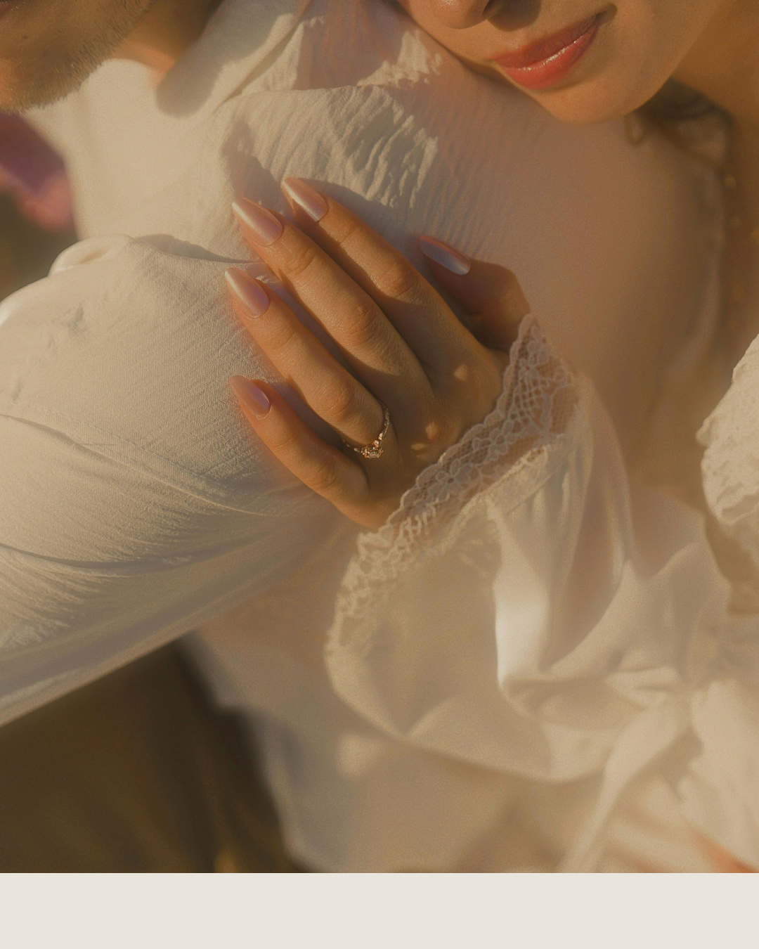 Close-up of a hand with long nails resting on white fabric in warm, soft light.