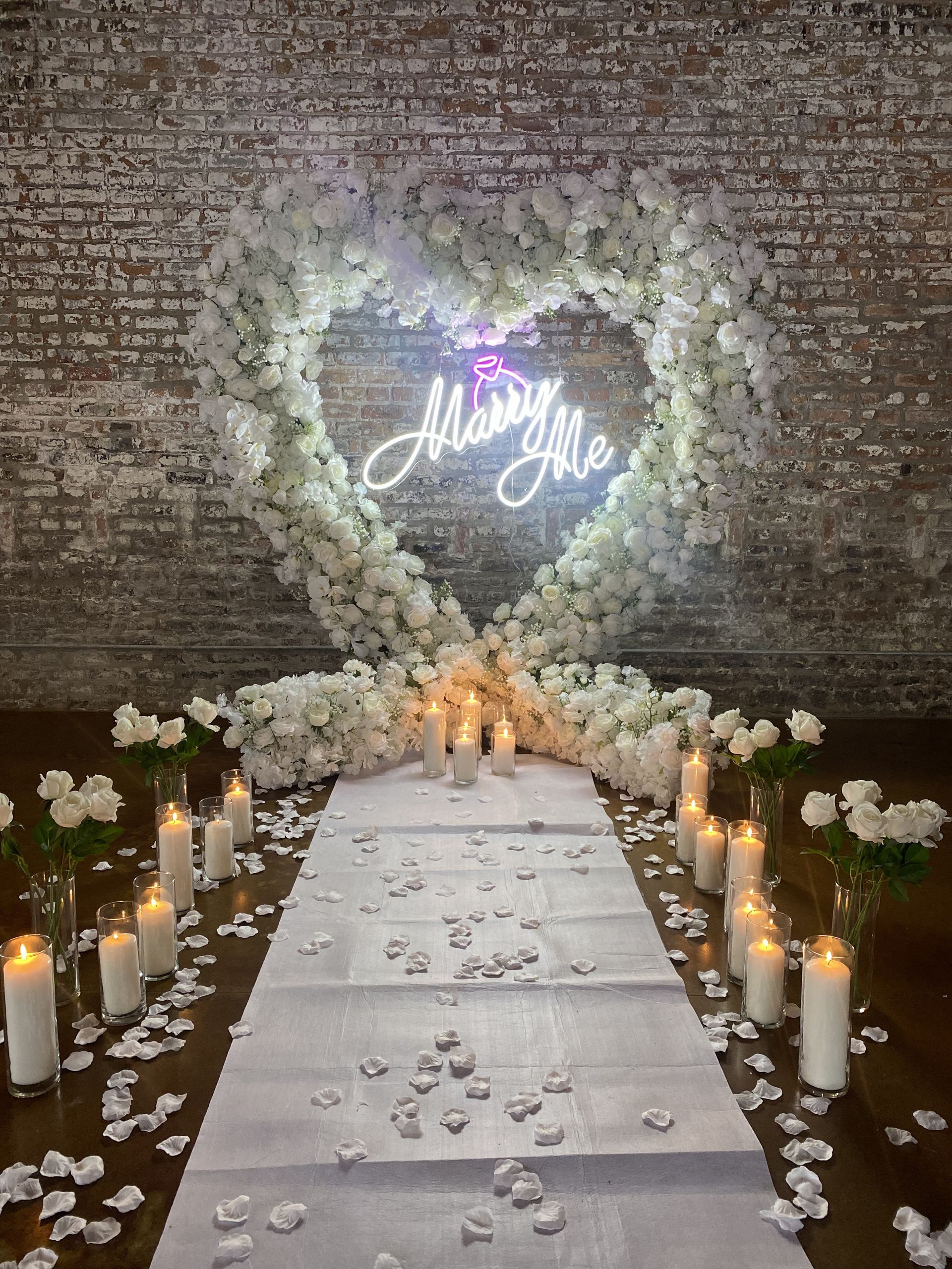 Romantic aisle with candles, white flowers, and glowing heart backdrop reading “Marry Me”