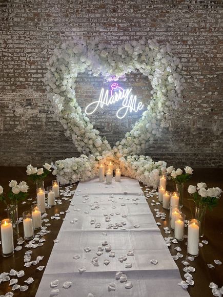 Romantic aisle with candles, white flowers, and glowing heart backdrop reading “Marry Me”