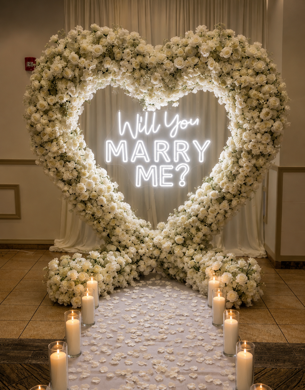 Heart-shaped white flower arch with neon “Will you marry me?” sign and candlelit aisle for a proposal