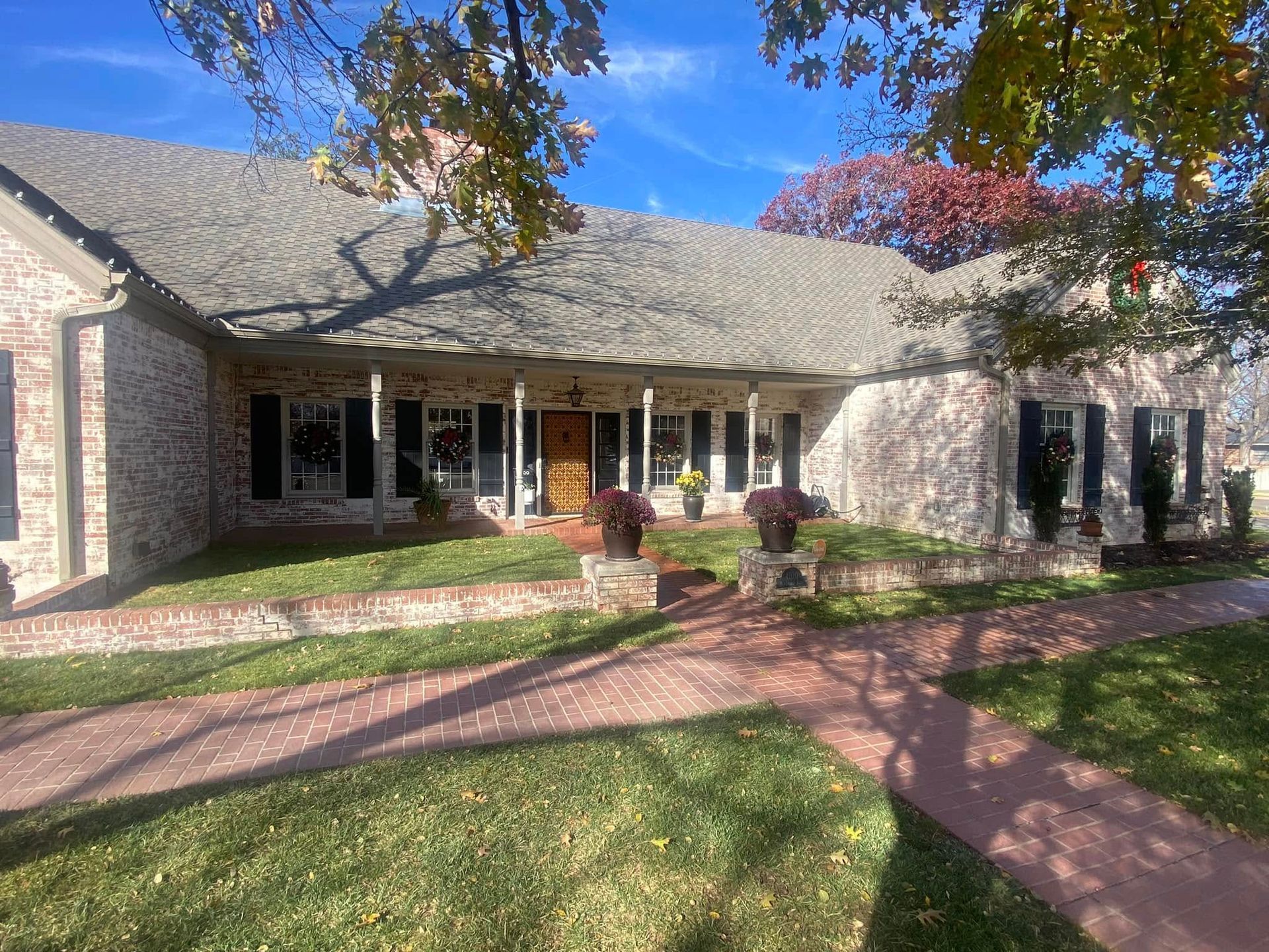Brick house with a covered porch, red brick walkway, and green lawn under a blue sky