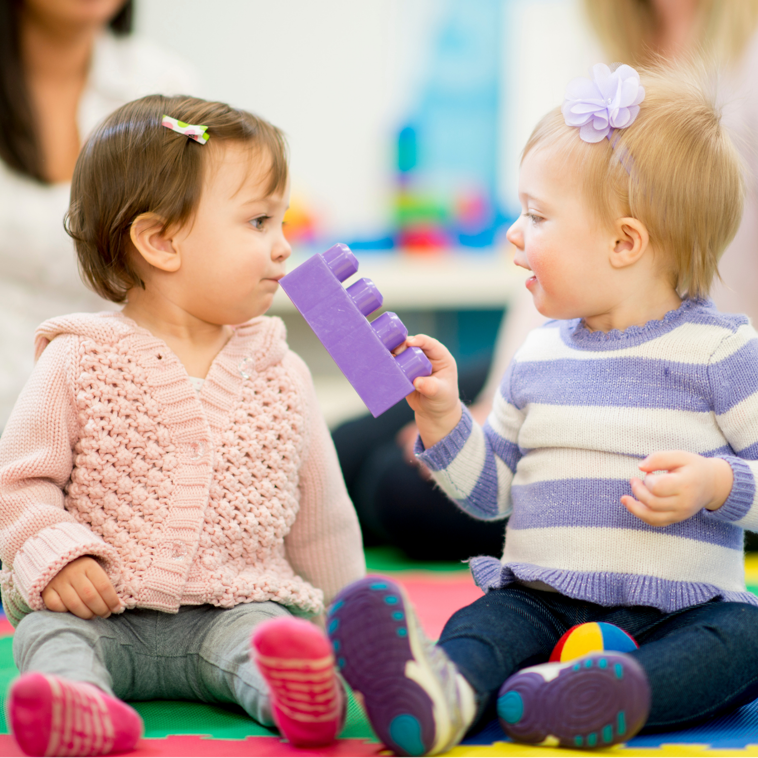 Two little girls are sitting on the floor playing with toys
