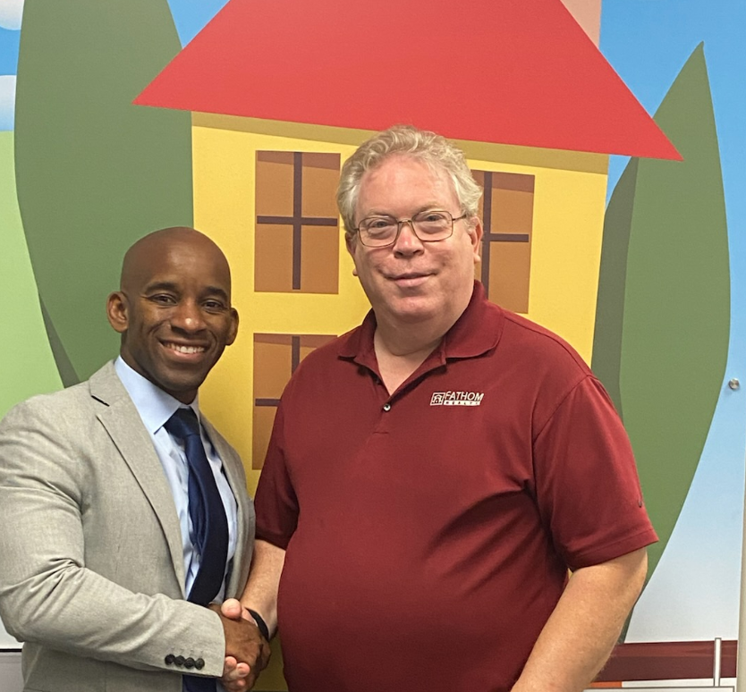 Two men shaking hands in front of a colorful house mural