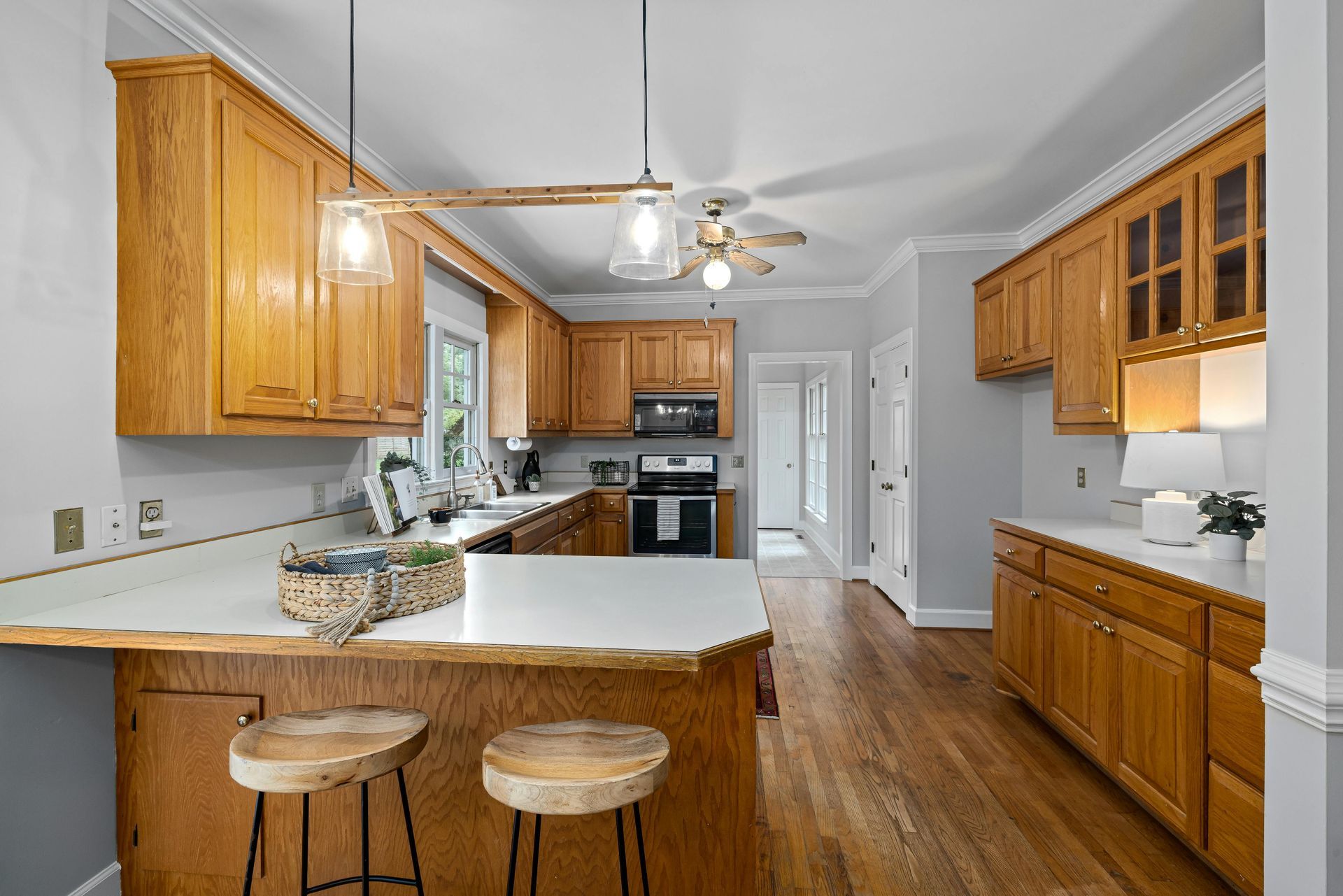 A kitchen with wooden cabinets , stools , a stove , and a ceiling fan.