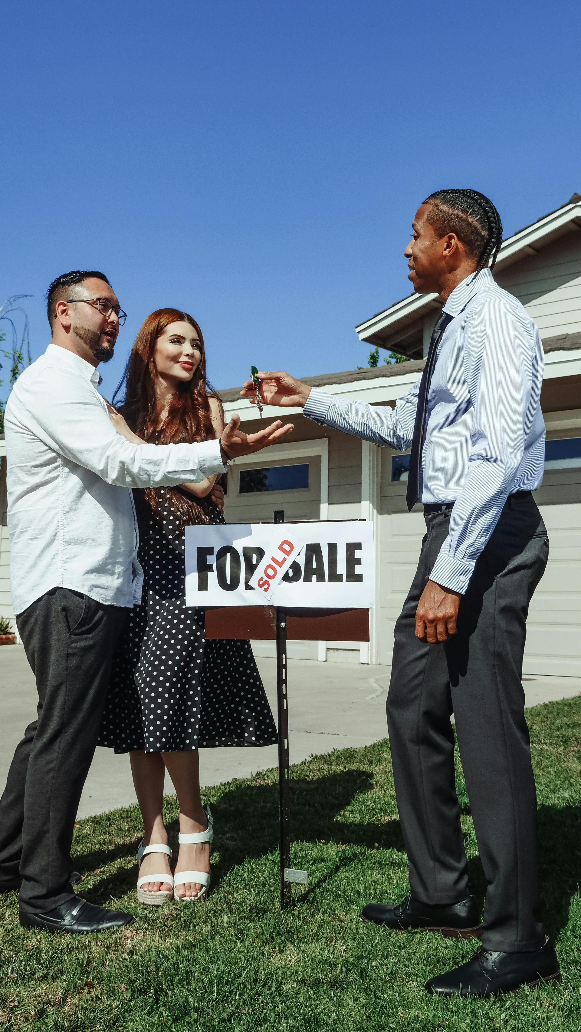 A real estate agent hands keys to a couple standing in front of a house with a